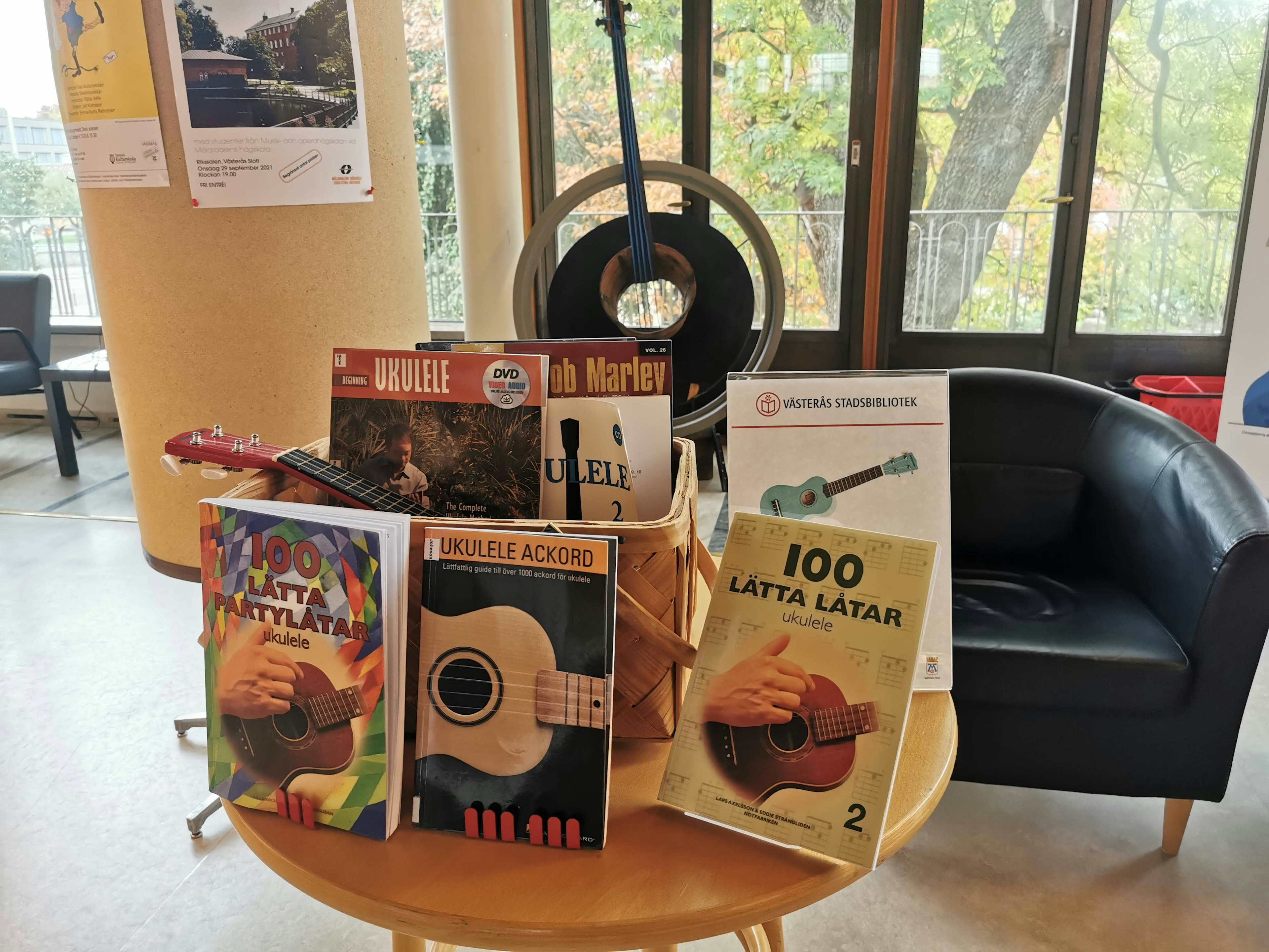 Libros de guitarra y partituras exhibidos en una mesa con una guitarra al fondo