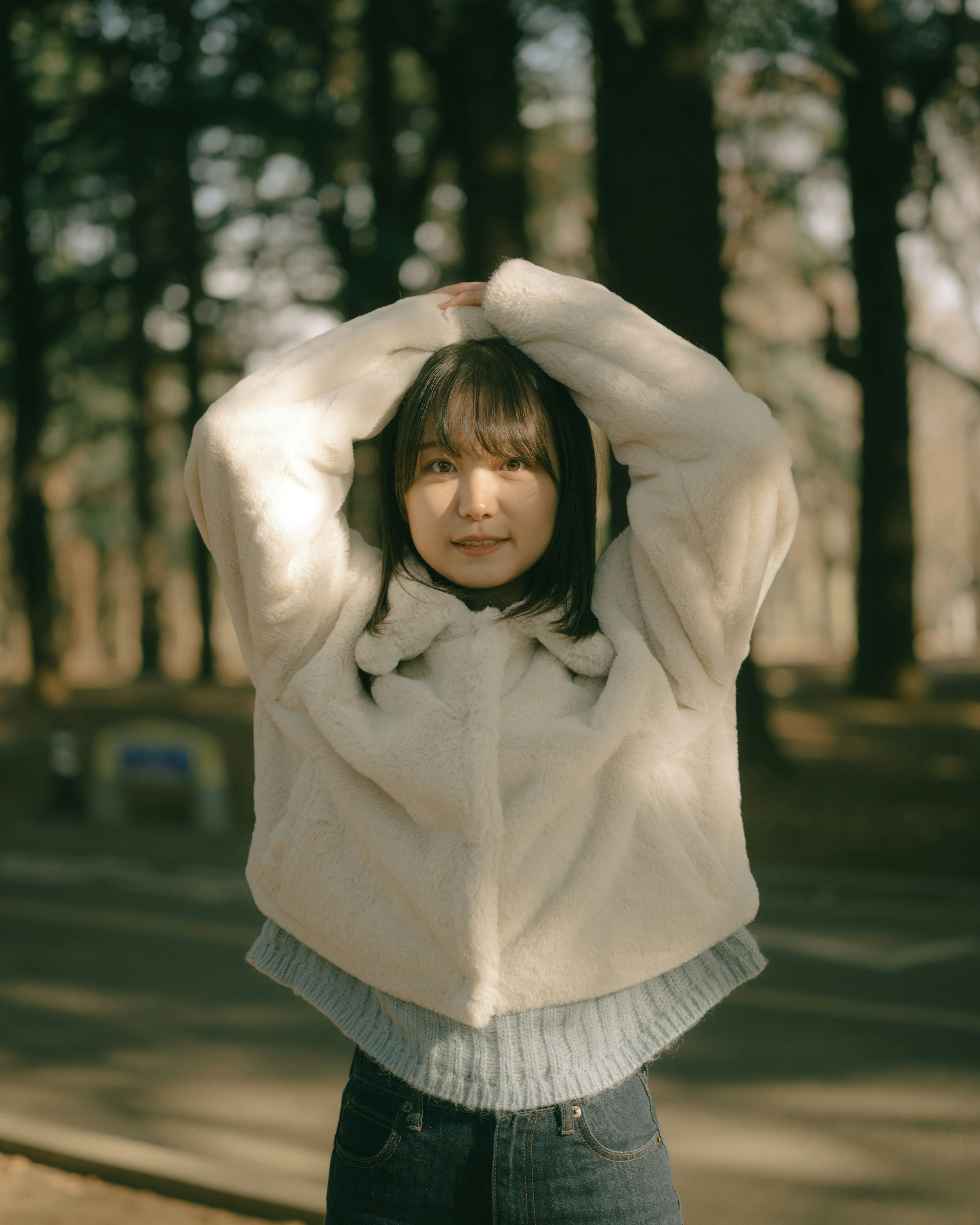 A woman in a white jacket raising her arms in a forest