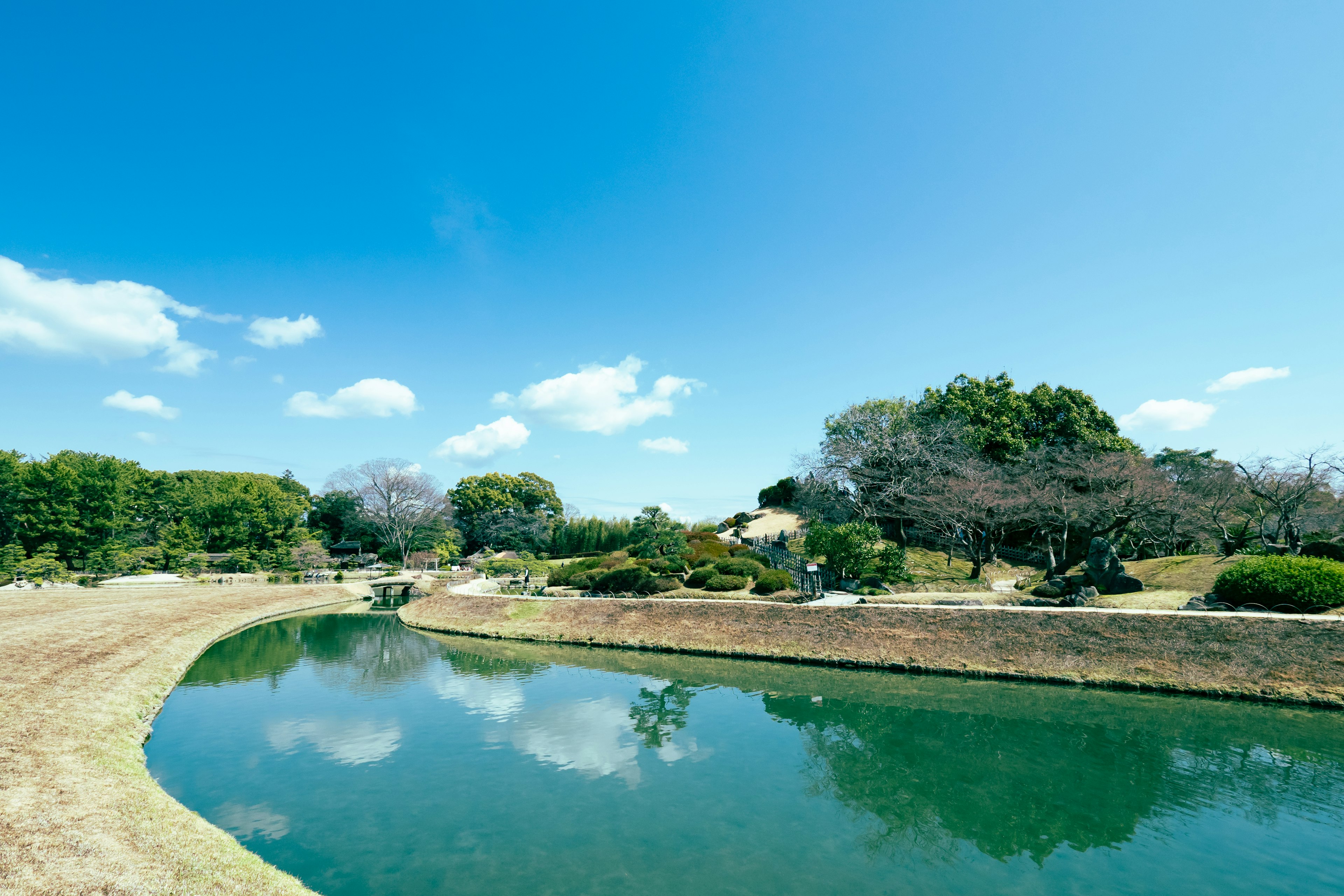 ทิวทัศน์สวนอันเงียบสงบที่มีท้องฟ้าสีฟ้าสดใสและการสะท้อนในน้ำ