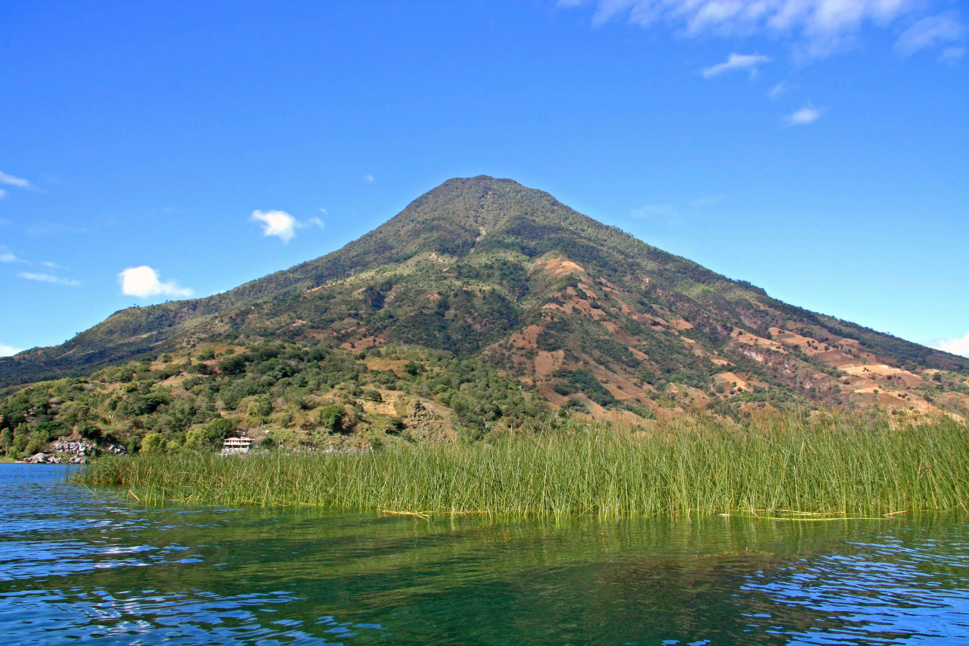 Vista pintoresca de un volcán que se eleva cerca de un lago con hierba verde exuberante