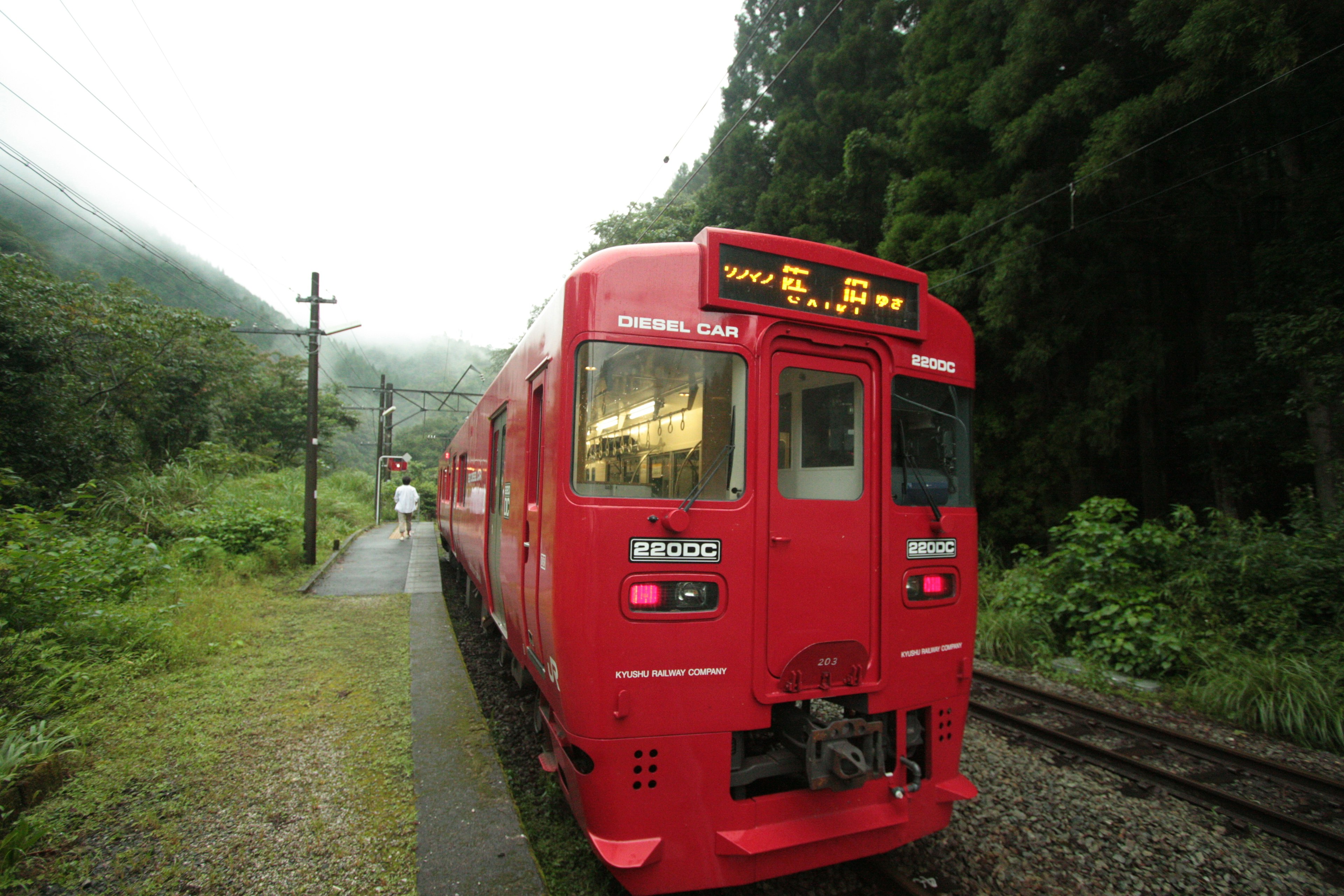 赤い列車が緑の木々に囲まれた線路に停車している