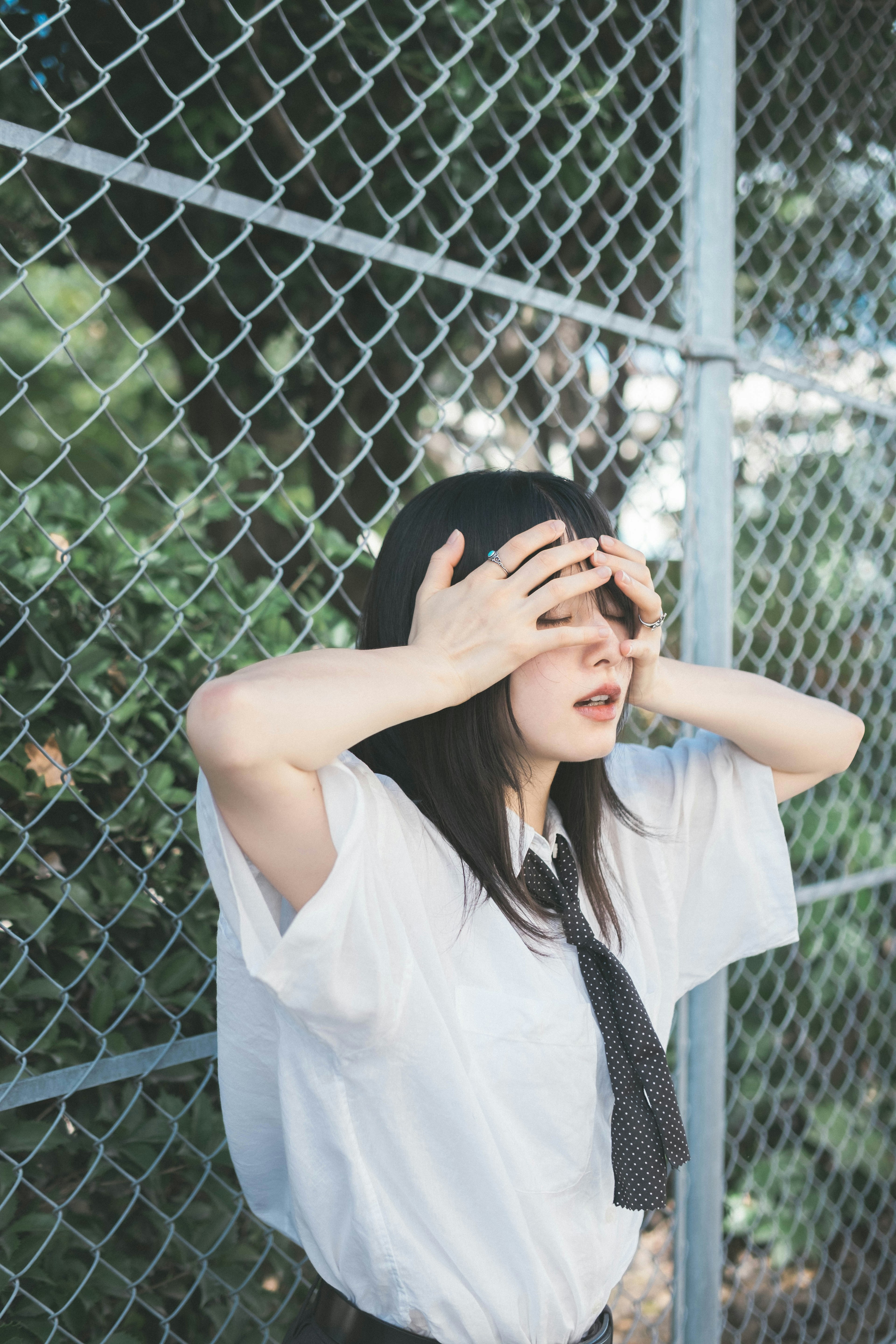 Woman covering her face with hands in front of a fence