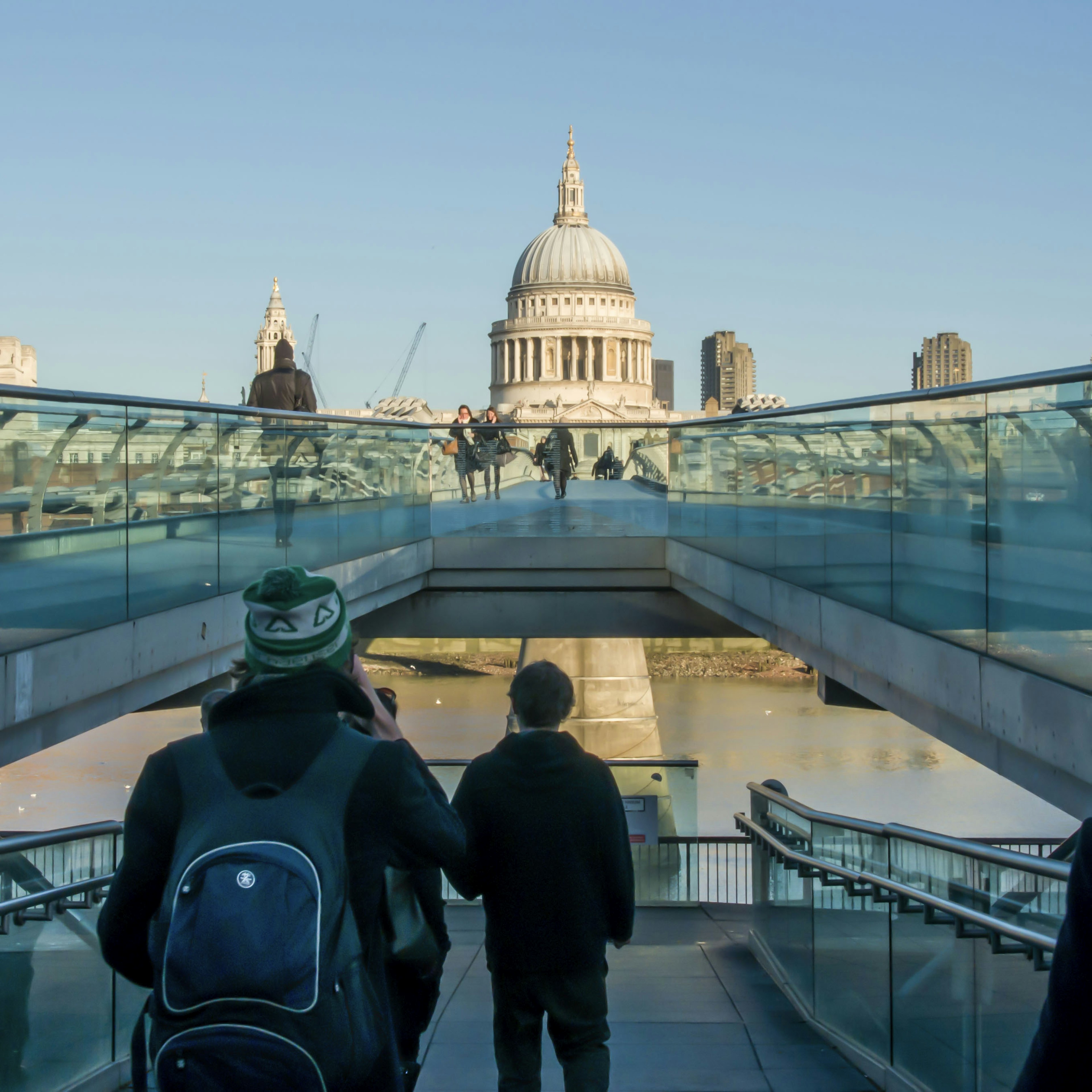 Personas caminando sobre un puente de vidrio con vista a la catedral de San Pablo