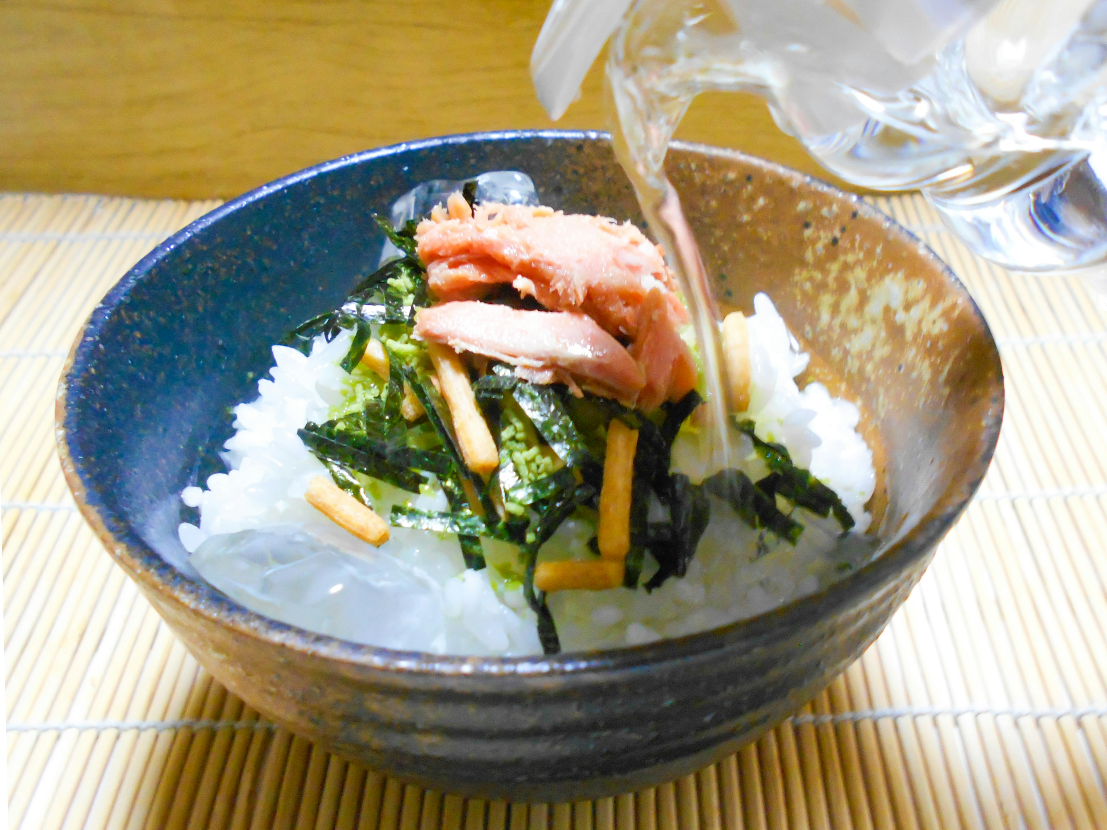 Un bol de riz garni d'algues et de saumon avec un liquide versé