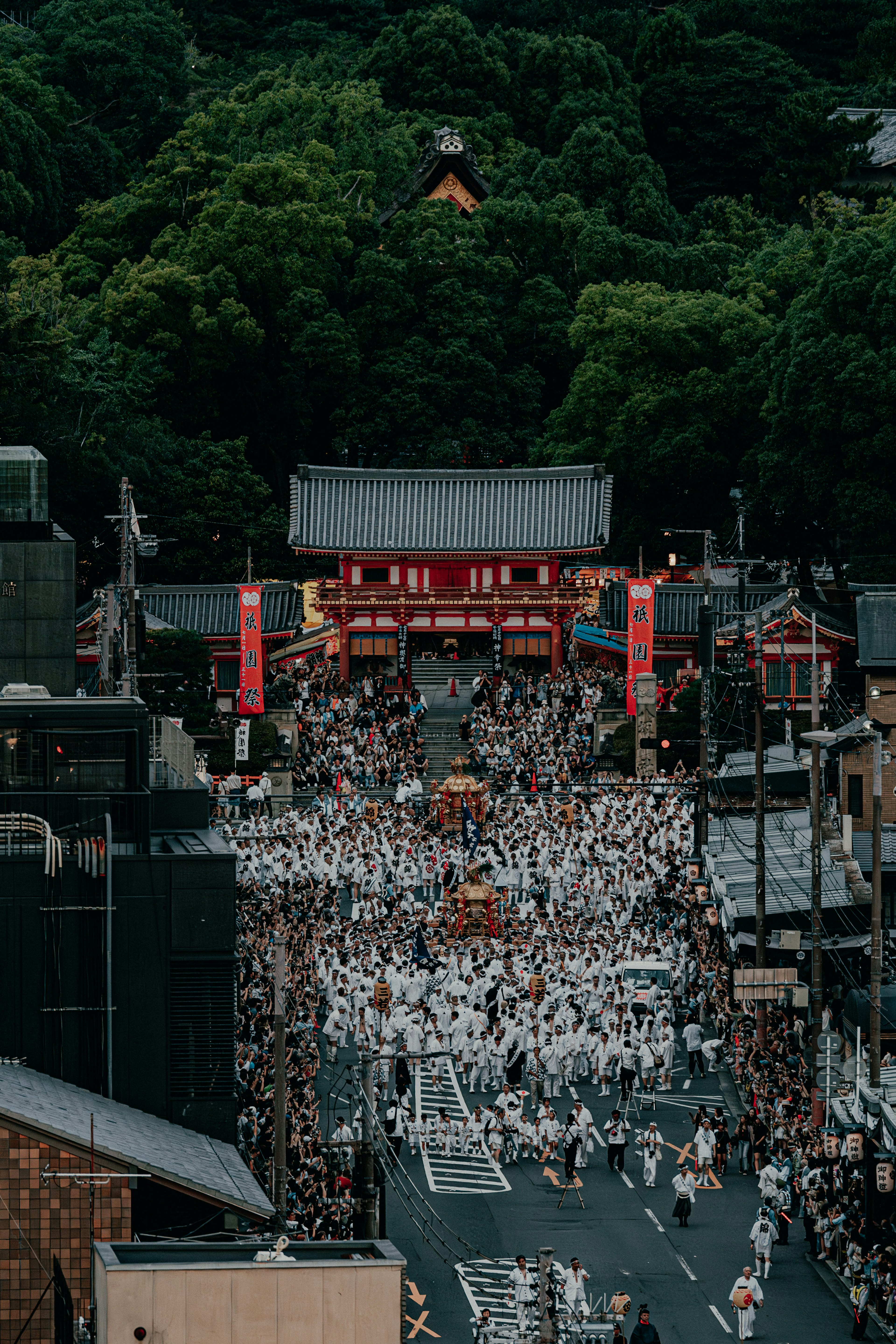 Procession de festival avec des personnes en tenue blanche devant une porte rouge entourée d'arbres verts