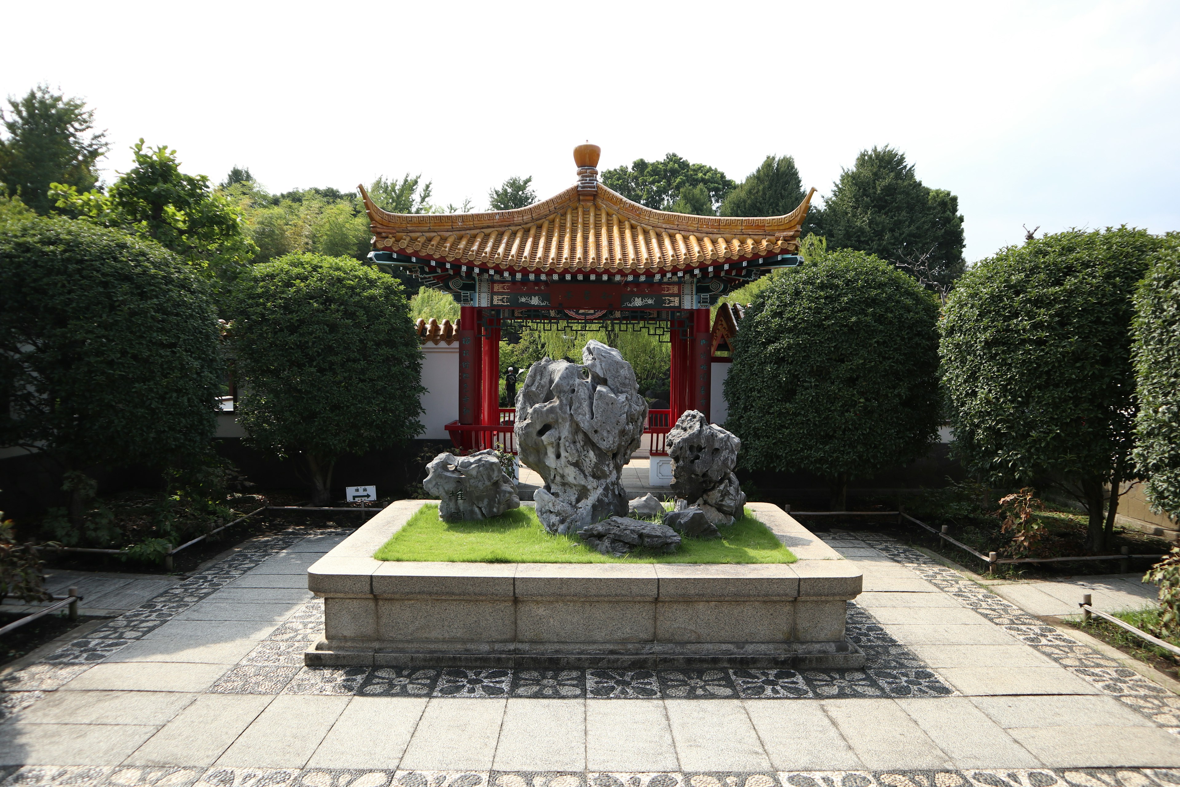 Steinskulptur im Zentrum eines Gartens mit traditionellem chinesischem Dachpavillon