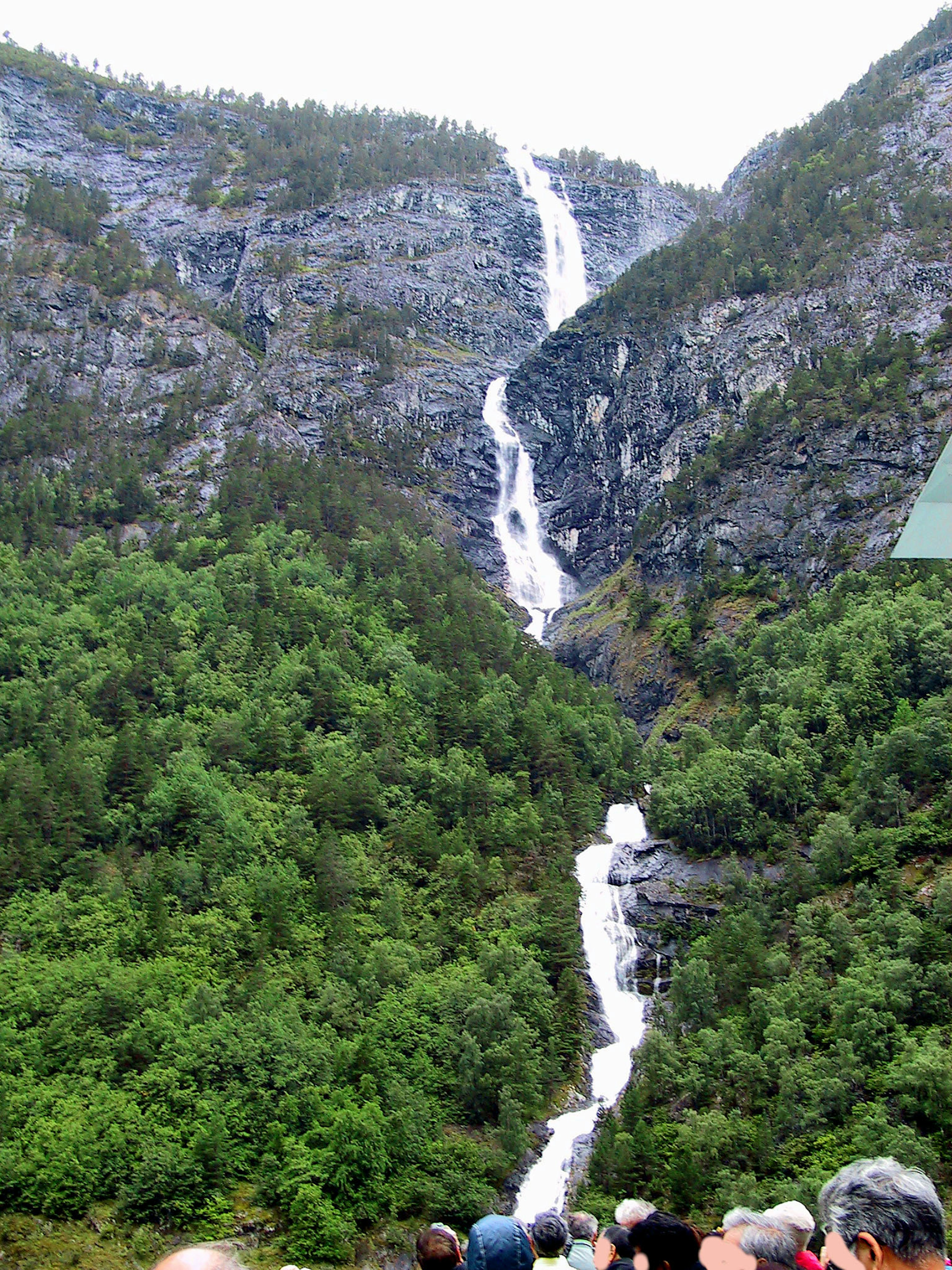 Majestätischer Wasserfall, der von felsigen Bergen umgeben von üppigem Grün herunterfällt, mit Menschen im Vordergrund