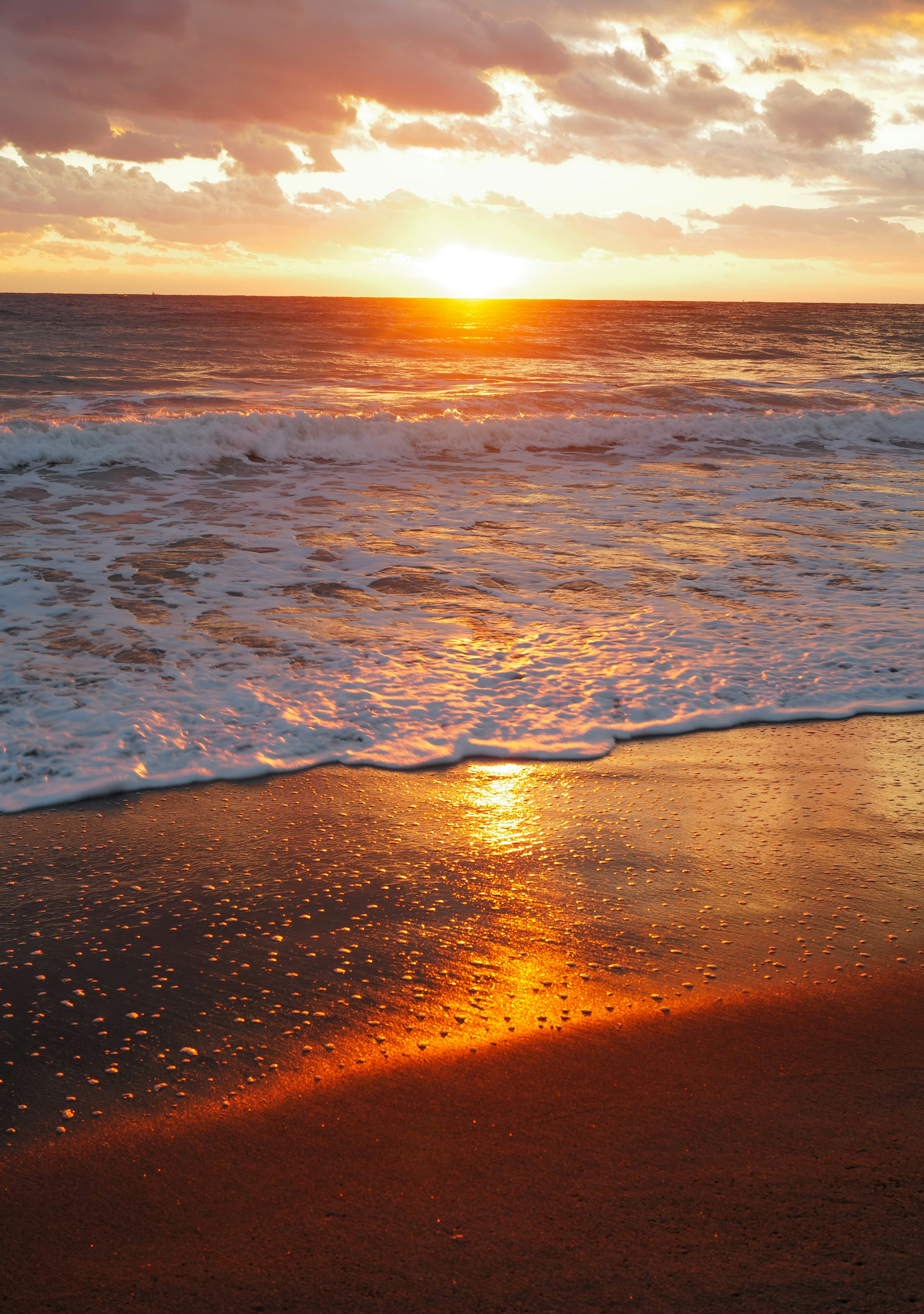 Escena de playa con un atardecer reflejándose en las olas del océano