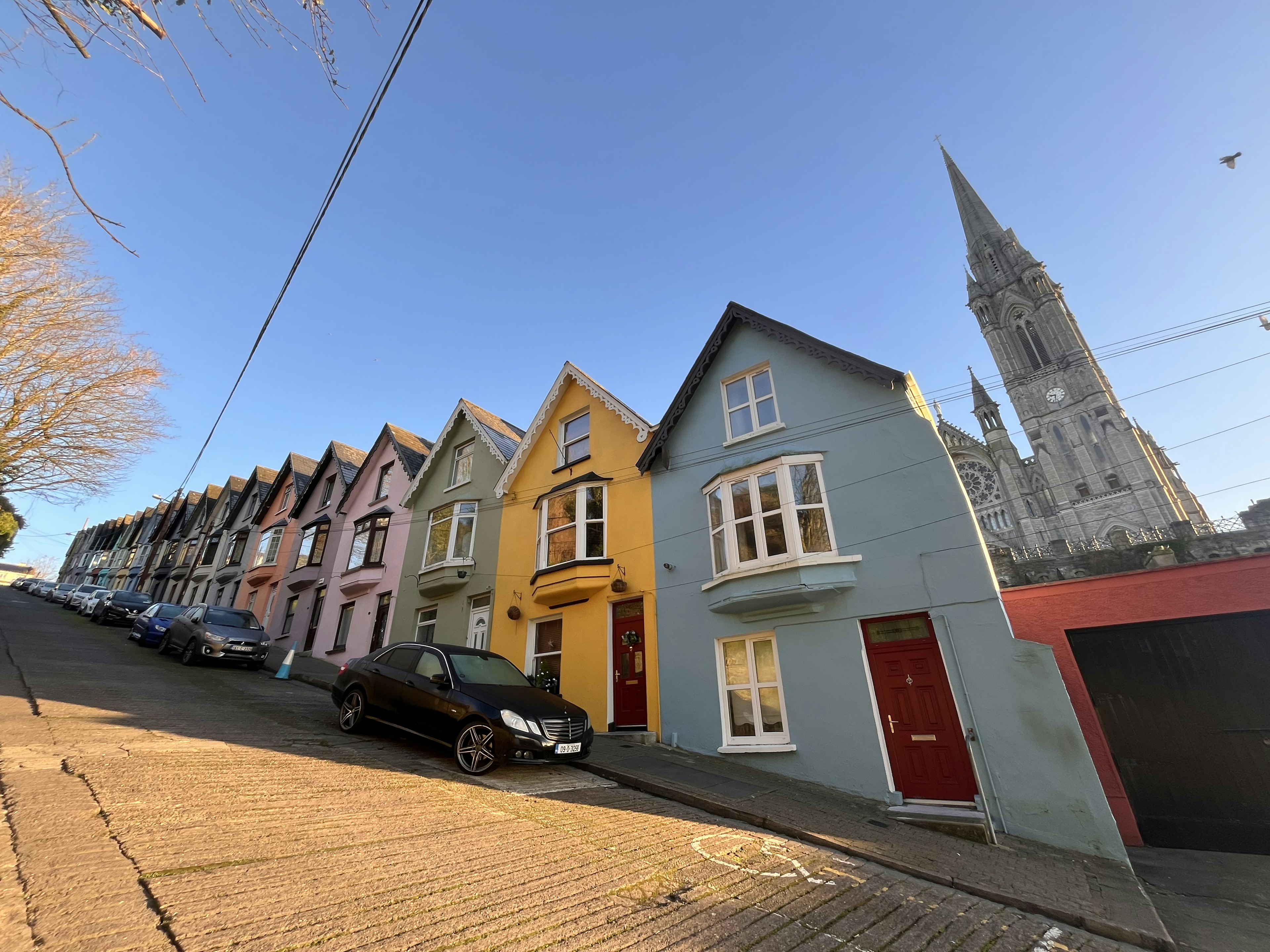 Colorful row of houses on a sloped street with a church tower in the background