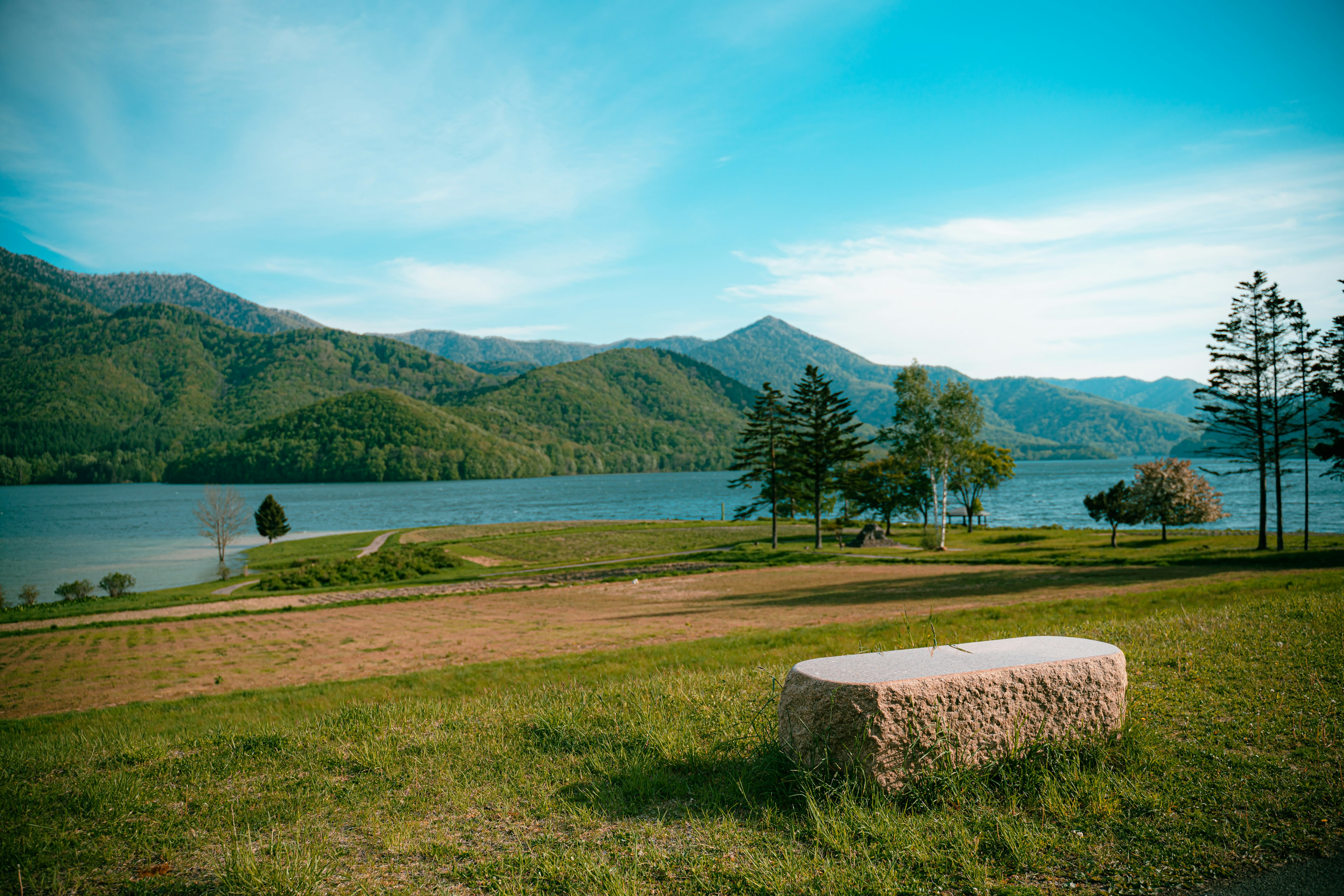 Vue pittoresque des montagnes verdoyantes entourant un lac sous un ciel bleu avec un banc en pierre au premier plan