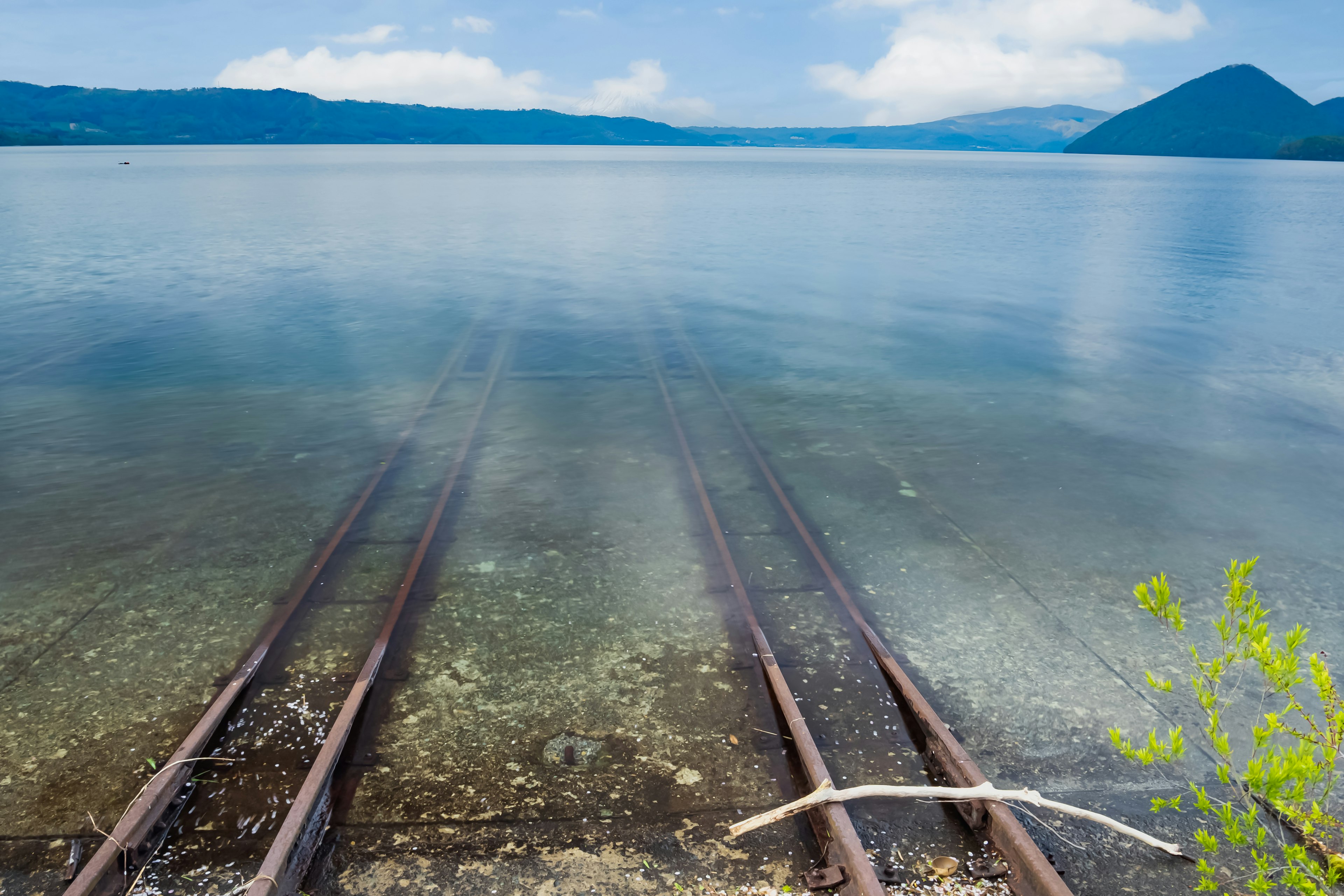 Rel kereta api terendam di danau dengan langit biru yang cerah