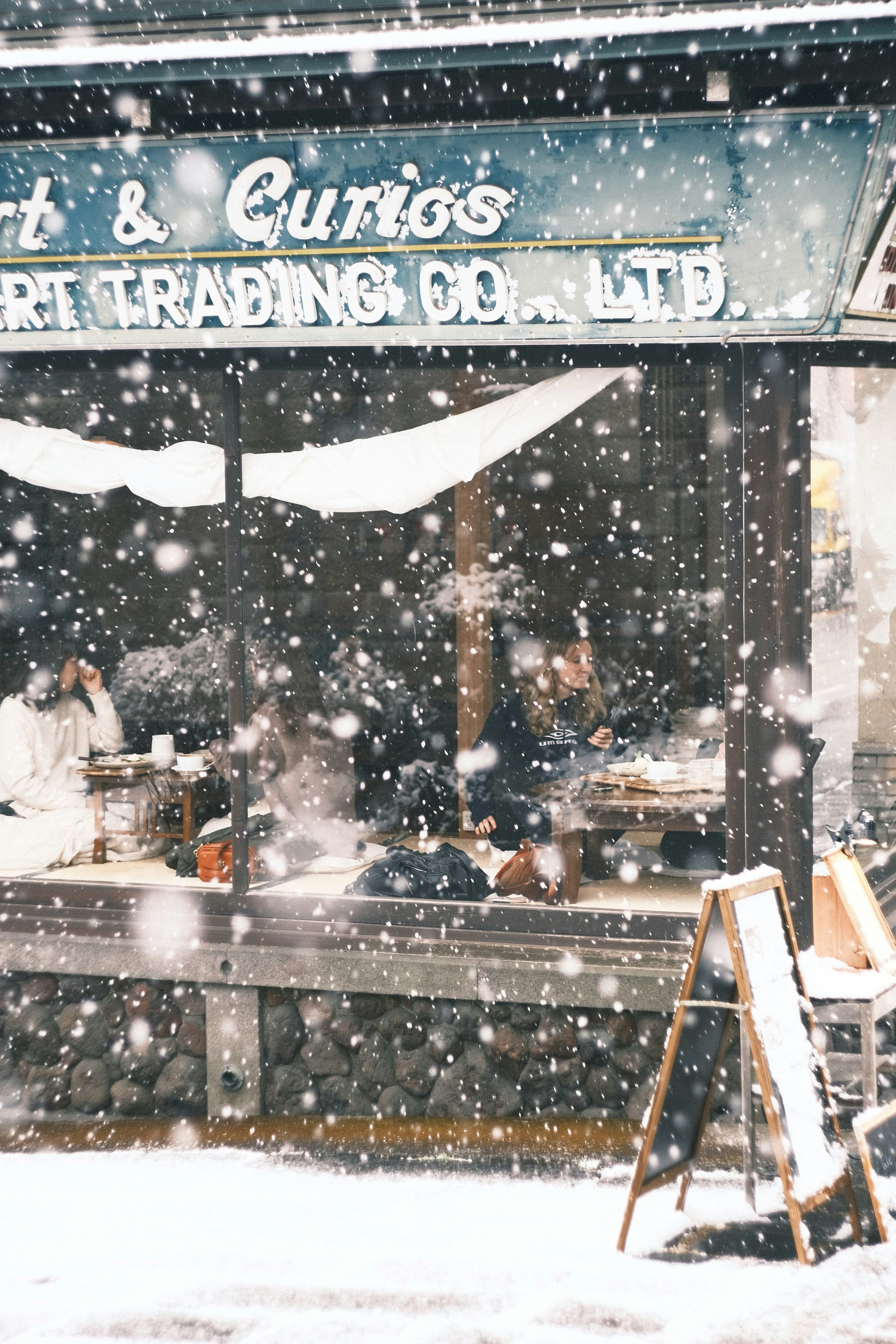 Exterior of an antique shop during snowfall with a sign