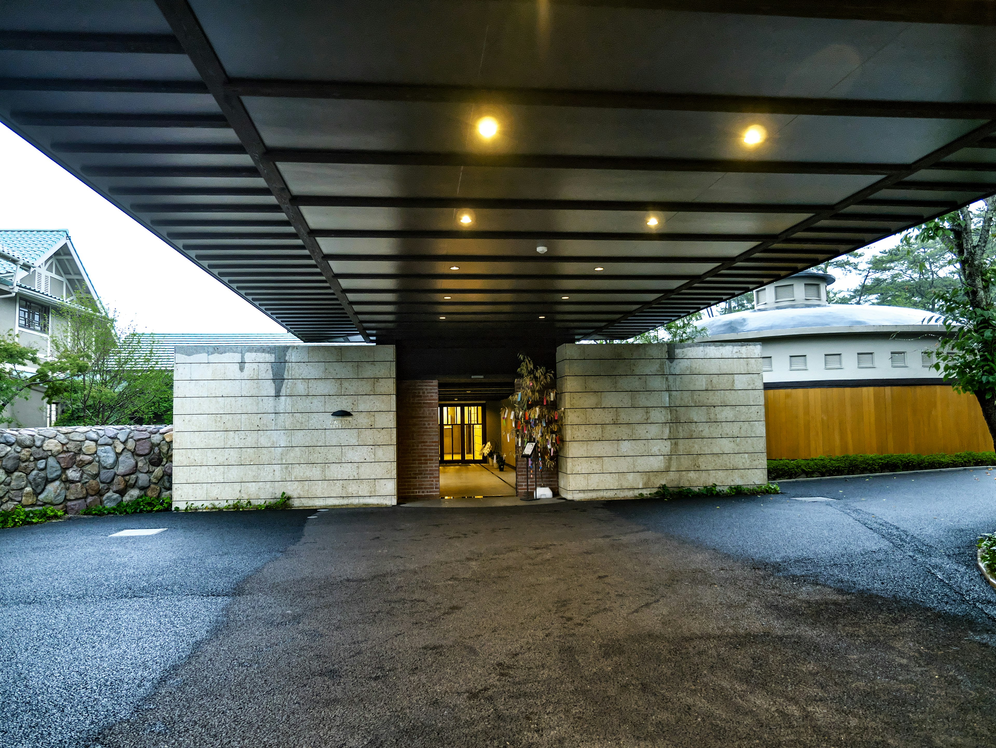 Modern entrance with a covered drive featuring bright lighting stone walls and green landscaping