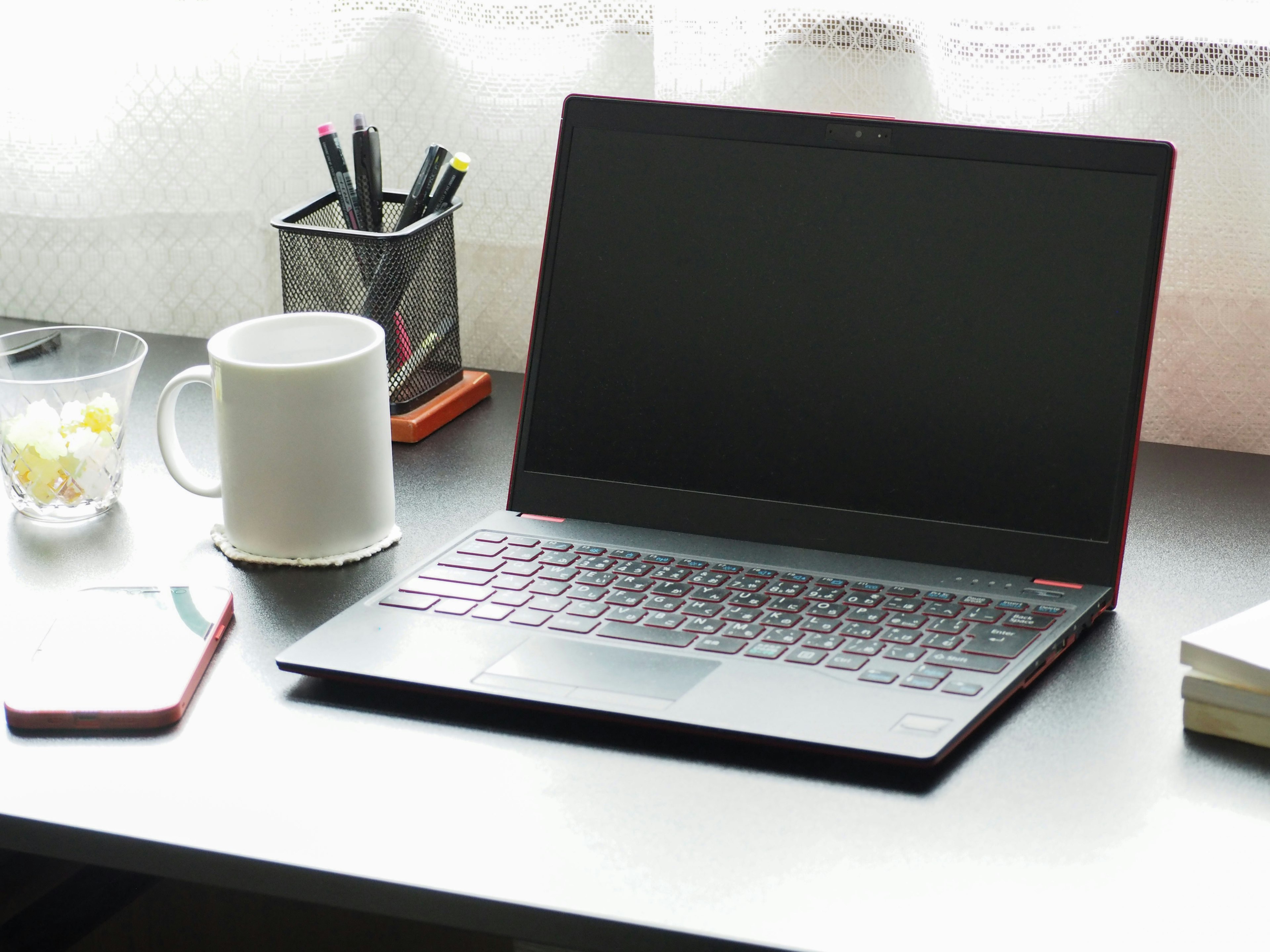 Una laptop roja en un escritorio con una taza blanca y un vaso de agua