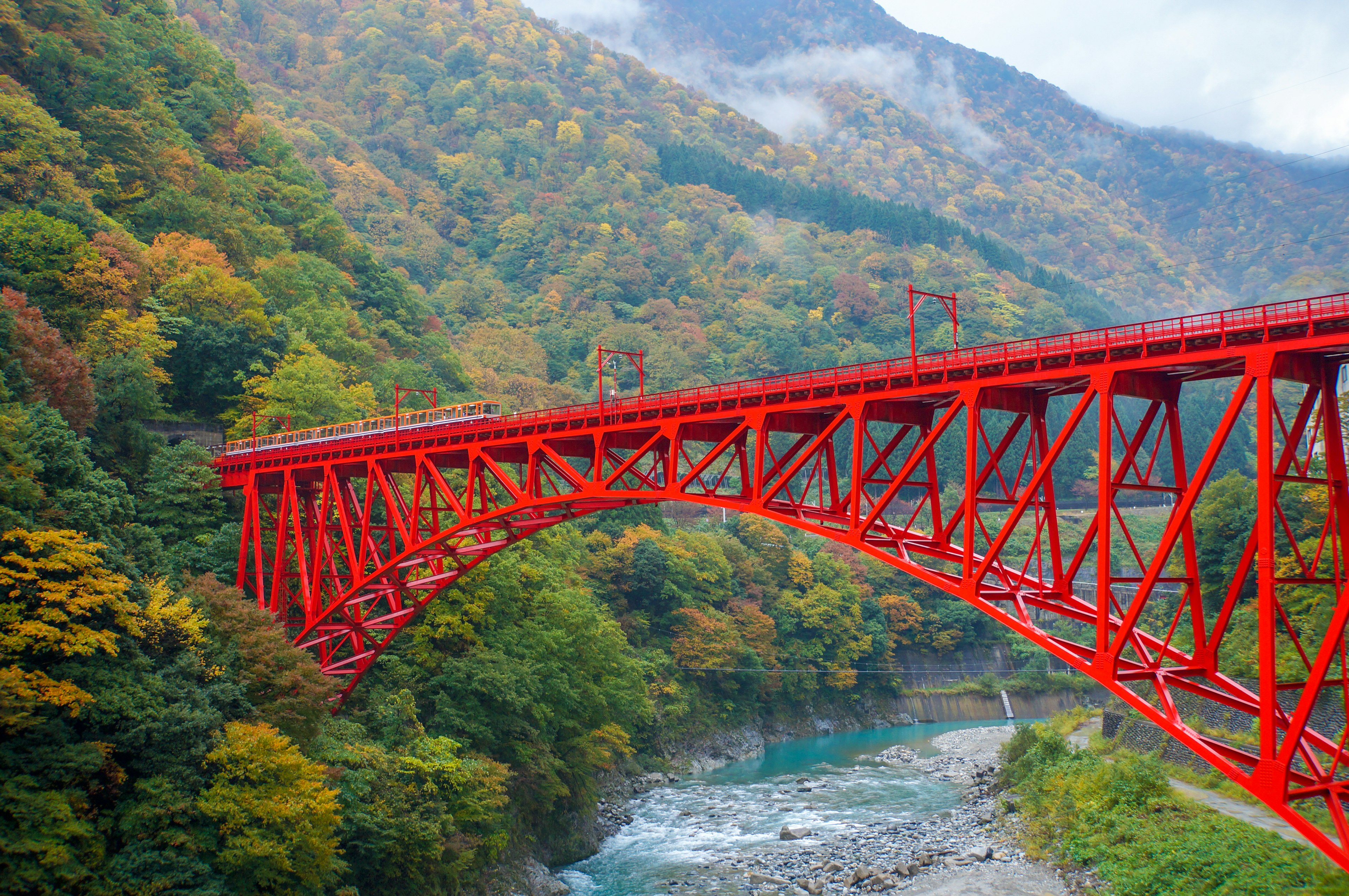 Red iron bridge in autumn landscape with green mountains