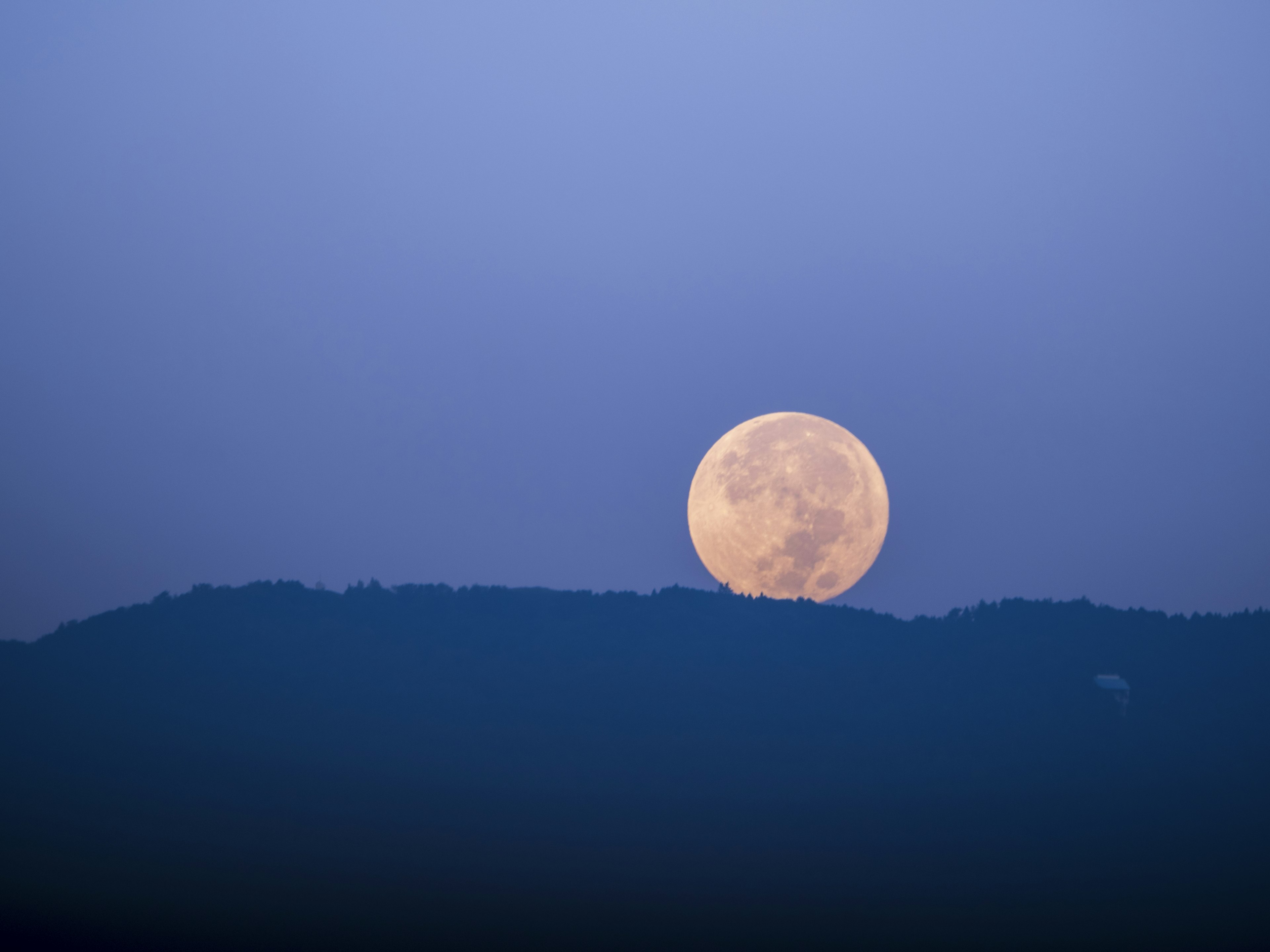 Grande luna piena che sorge sopra il profilo di una montagna contro un cielo blu