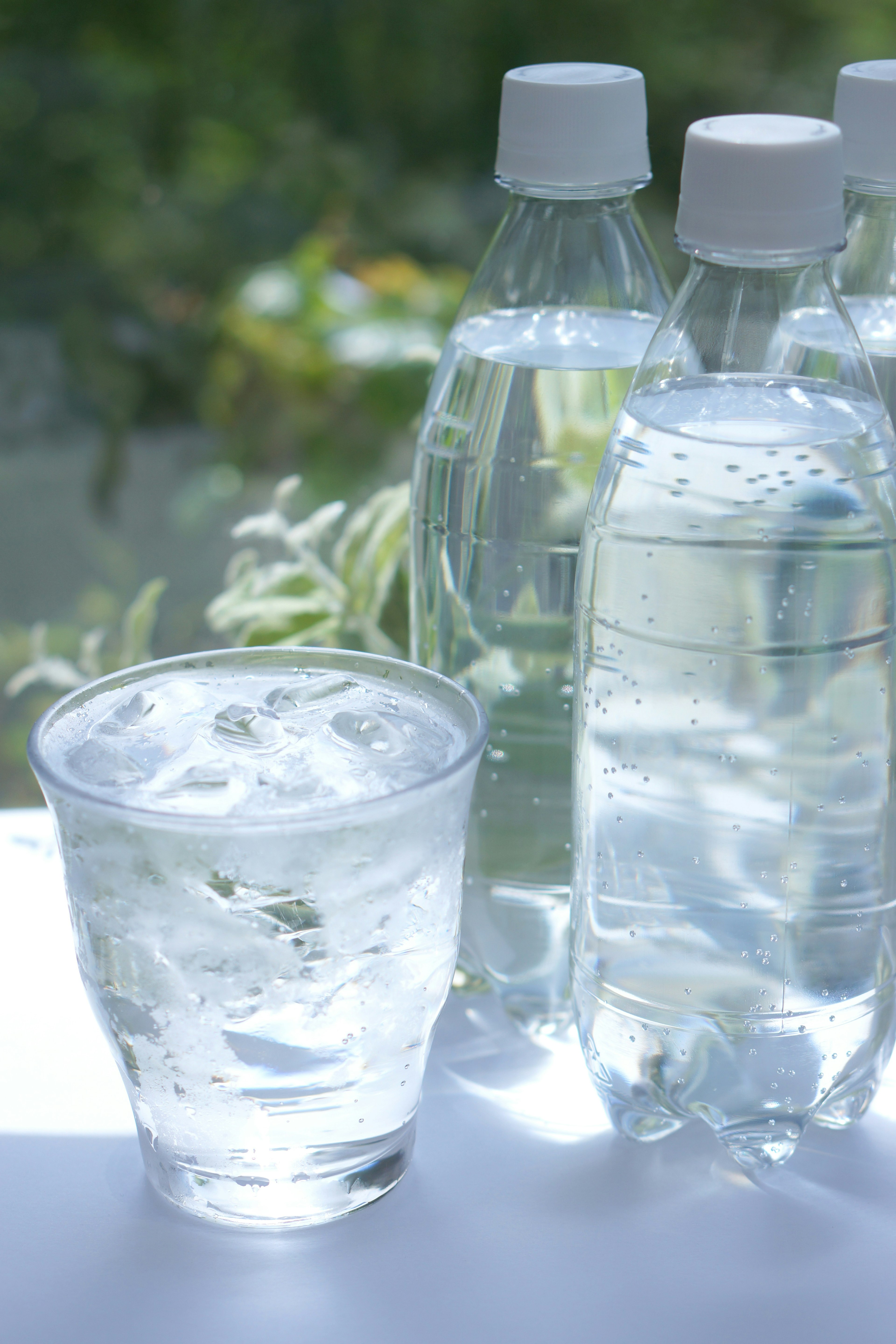 A glass filled with ice water alongside several plastic water bottles