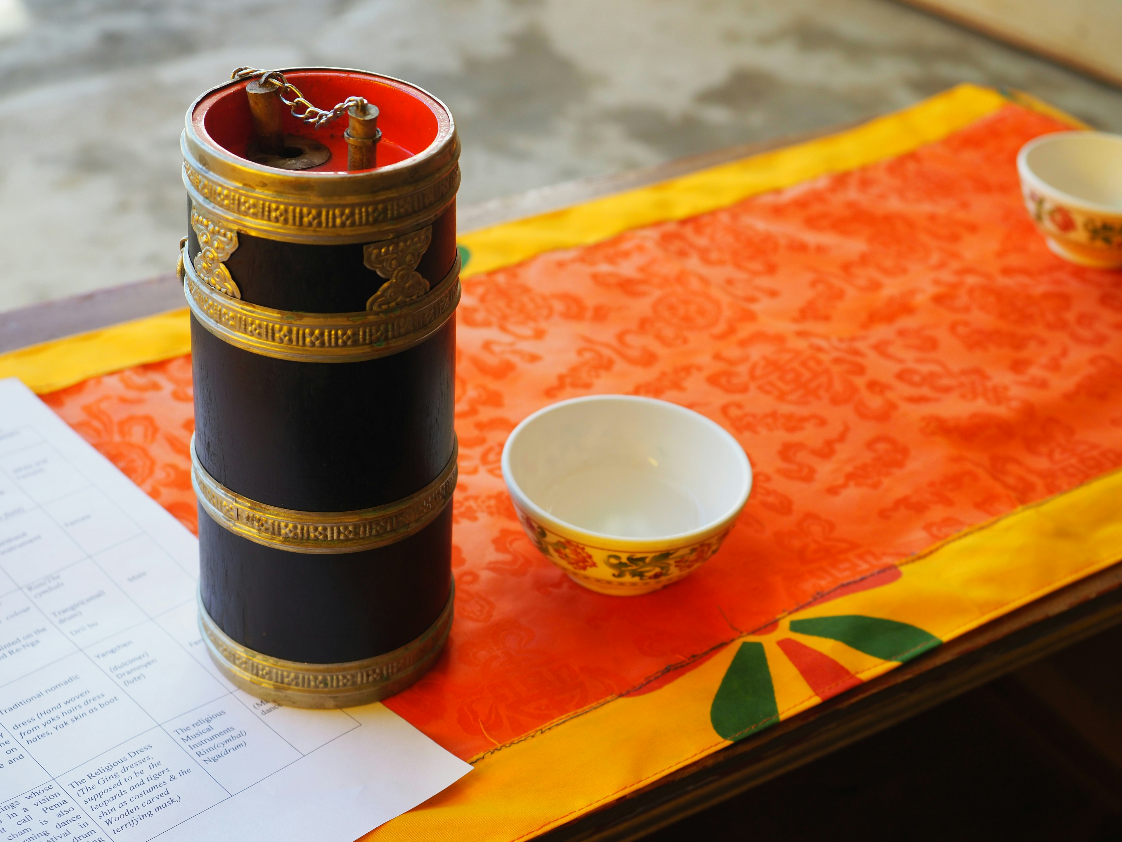 Decorative cylindrical container with red interior and two white bowls on an orange cloth