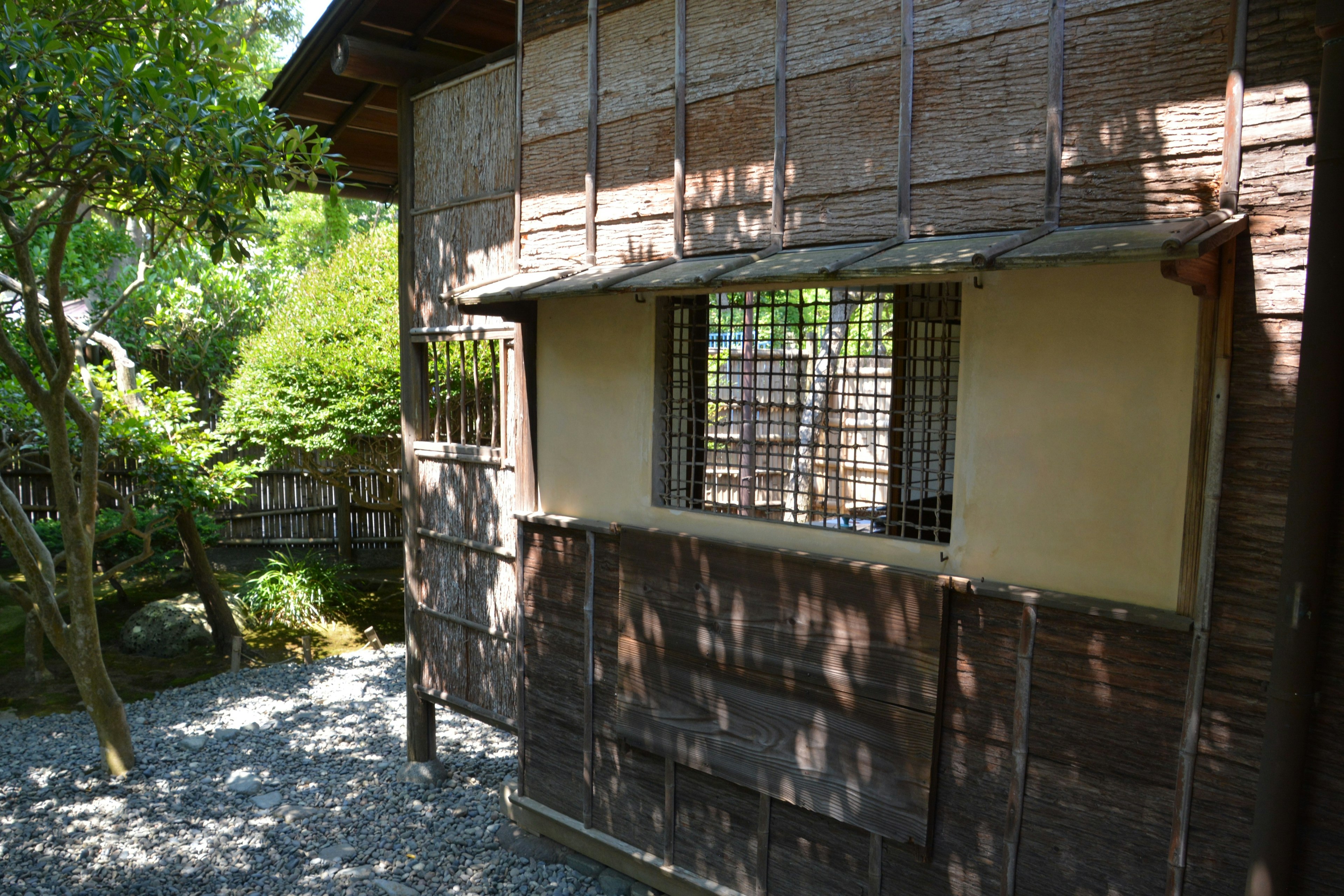 Exterior view of a traditional Japanese building surrounded by greenery featuring bamboo walls and a window