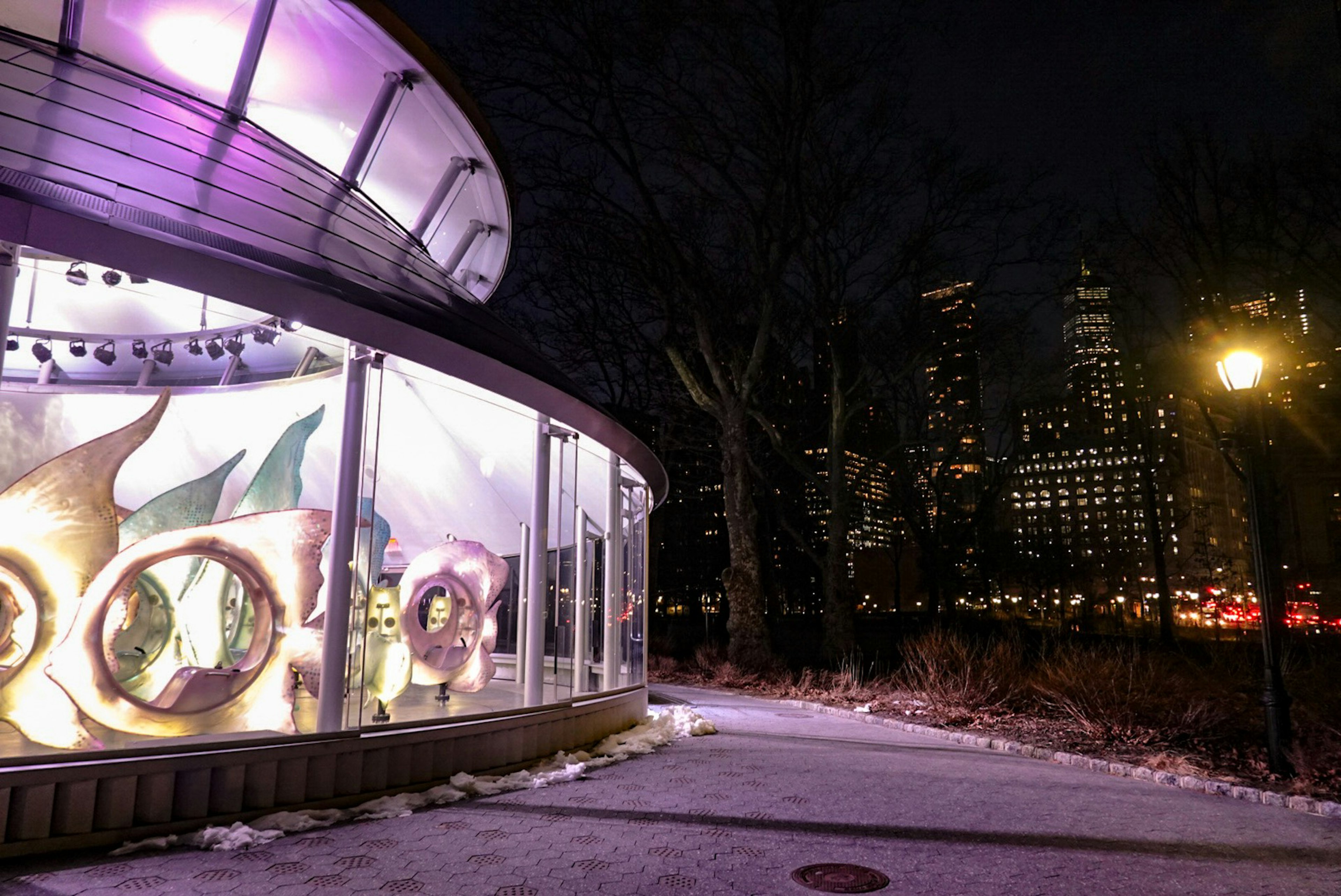 Espace d'exposition en verre illuminé en violet sur fond de skyline nocturne