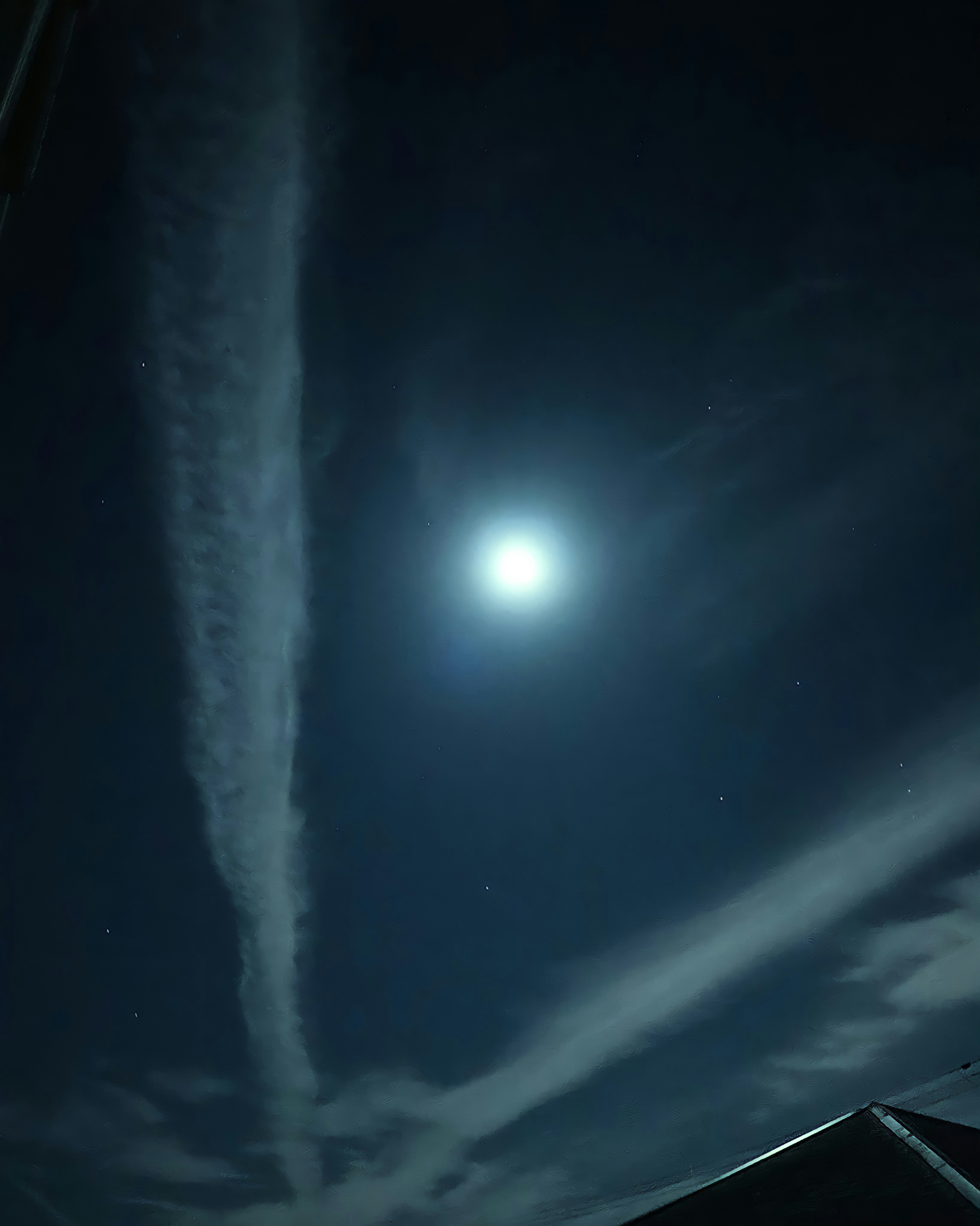 Bright moon shining in the night sky with cloud trails