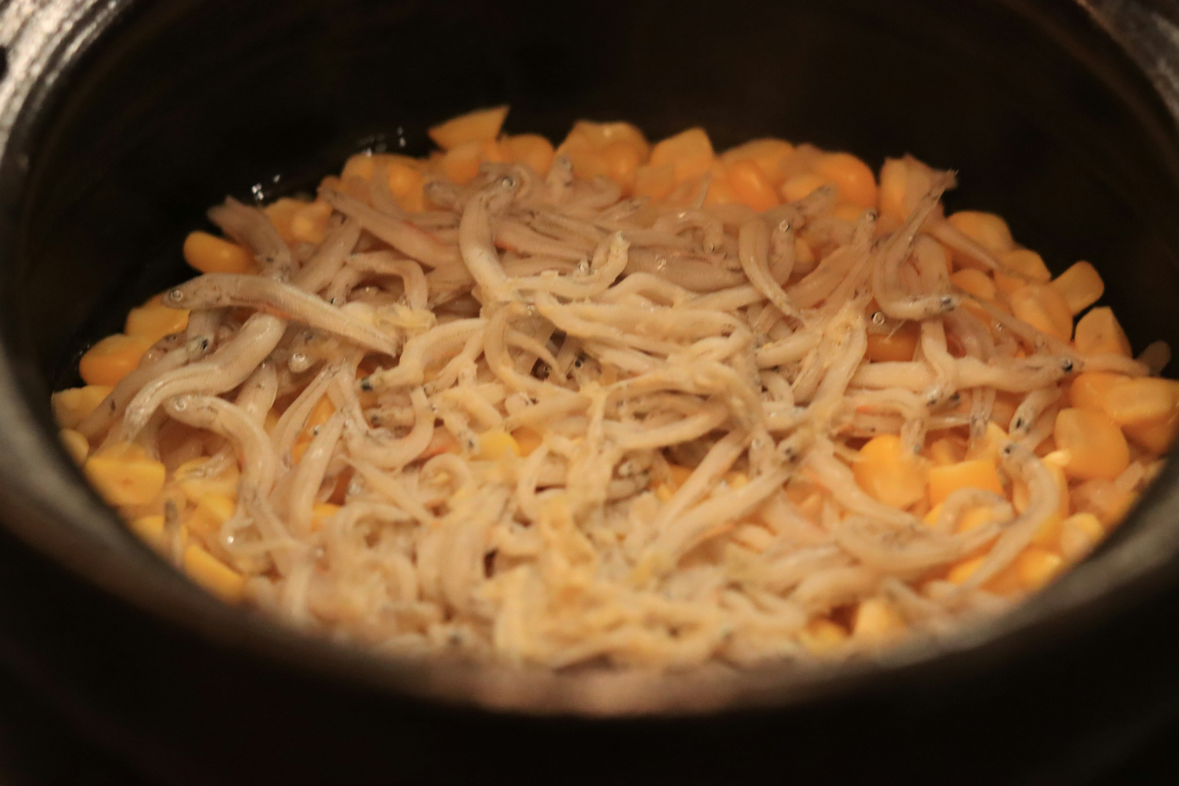 A dish in a pot featuring yellow ingredients and thin fish layered on top