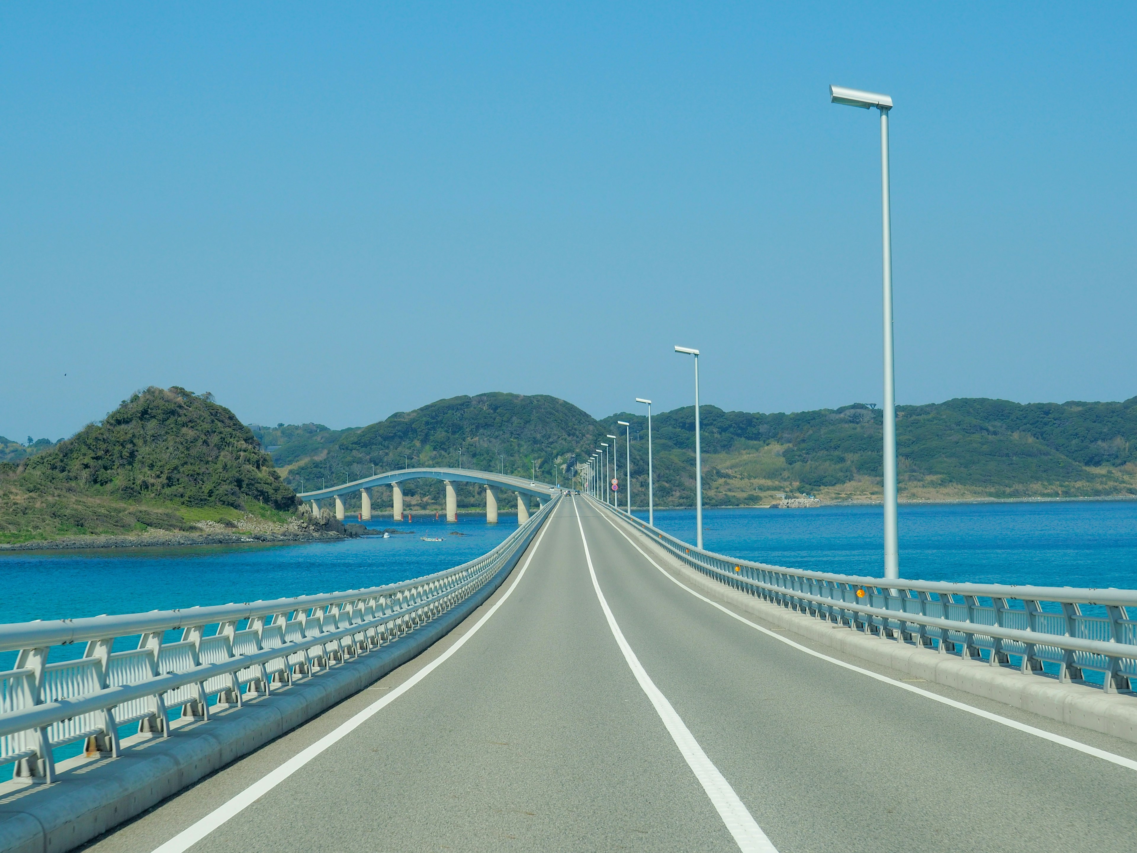 青い海に架かる長い橋と周囲の緑の丘