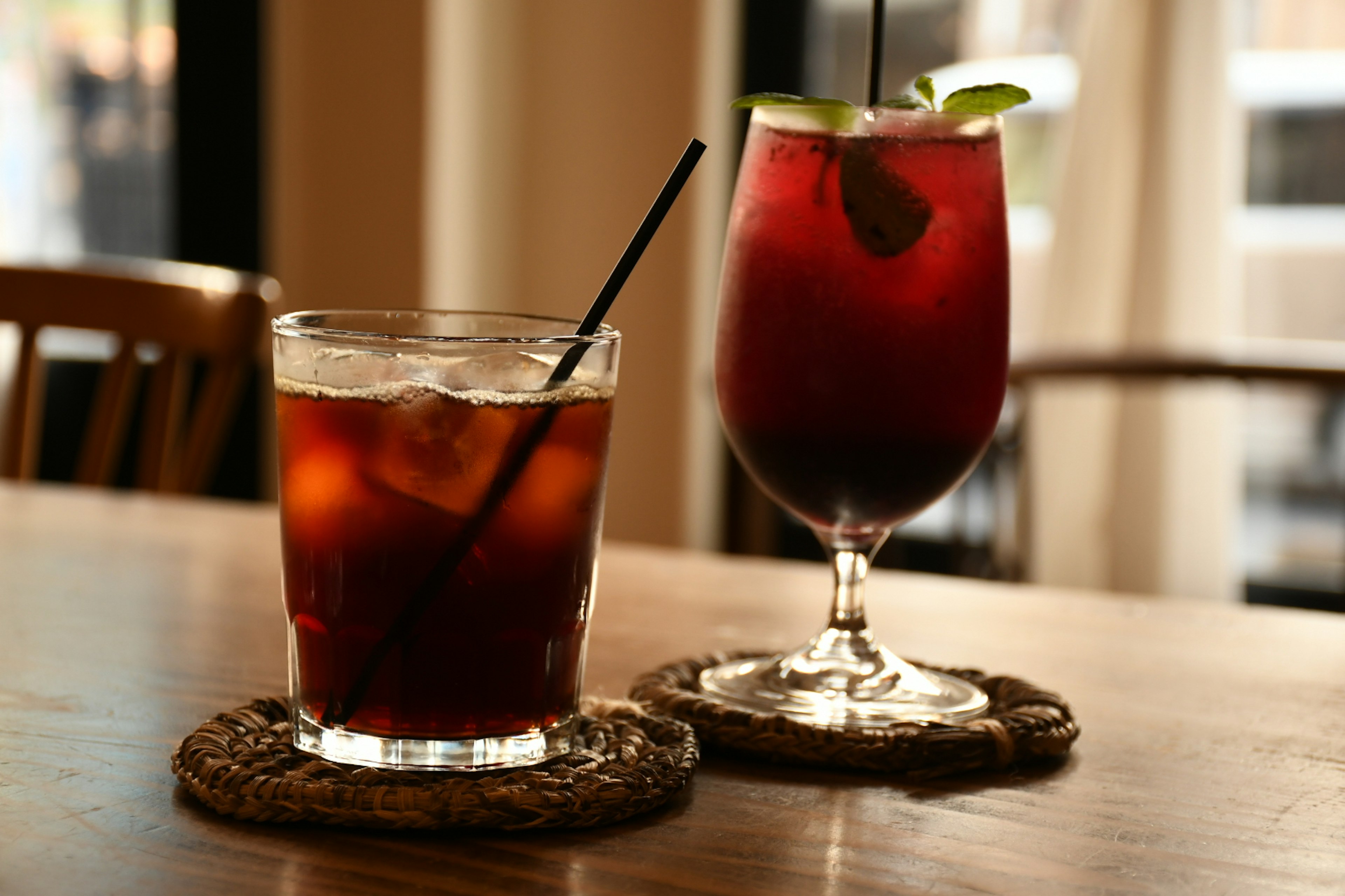 Deux boissons glacées sur une table, un verre à gauche avec de la glace et une boisson sombre, un verre à droite avec une boisson rouge et une garniture de citron vert