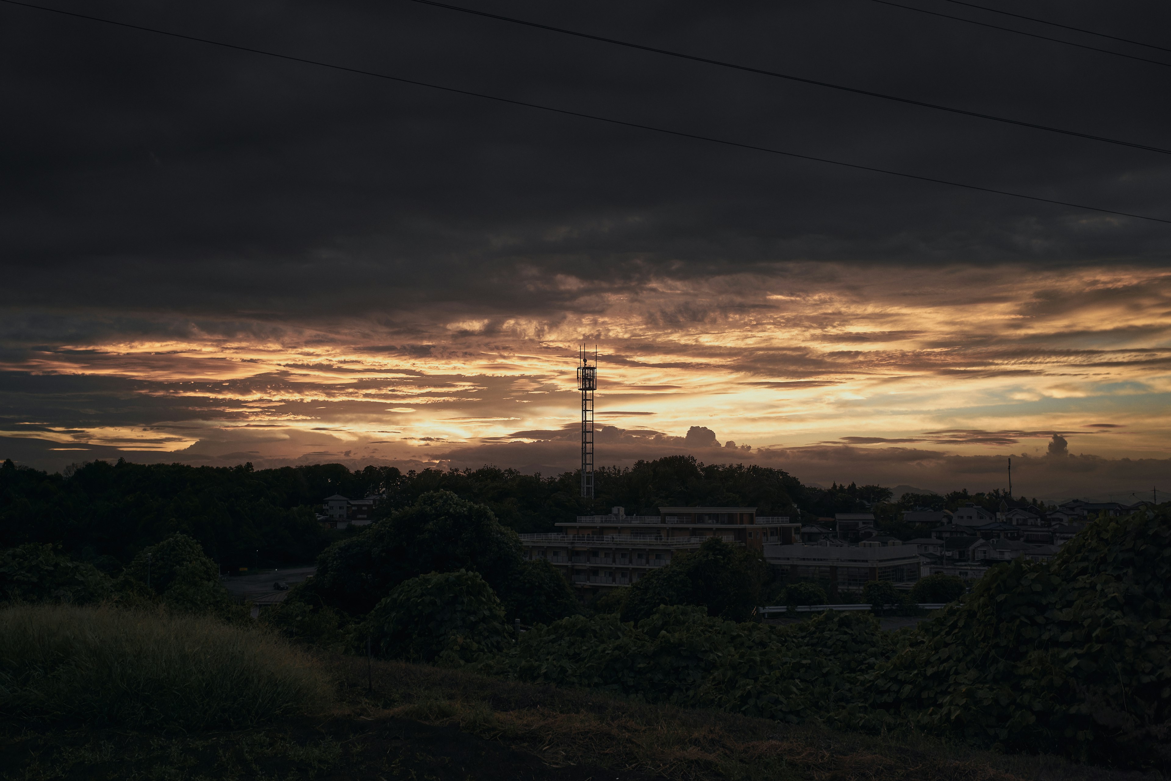 Landscape of a sunset under dark clouds with a tall communication tower silhouette