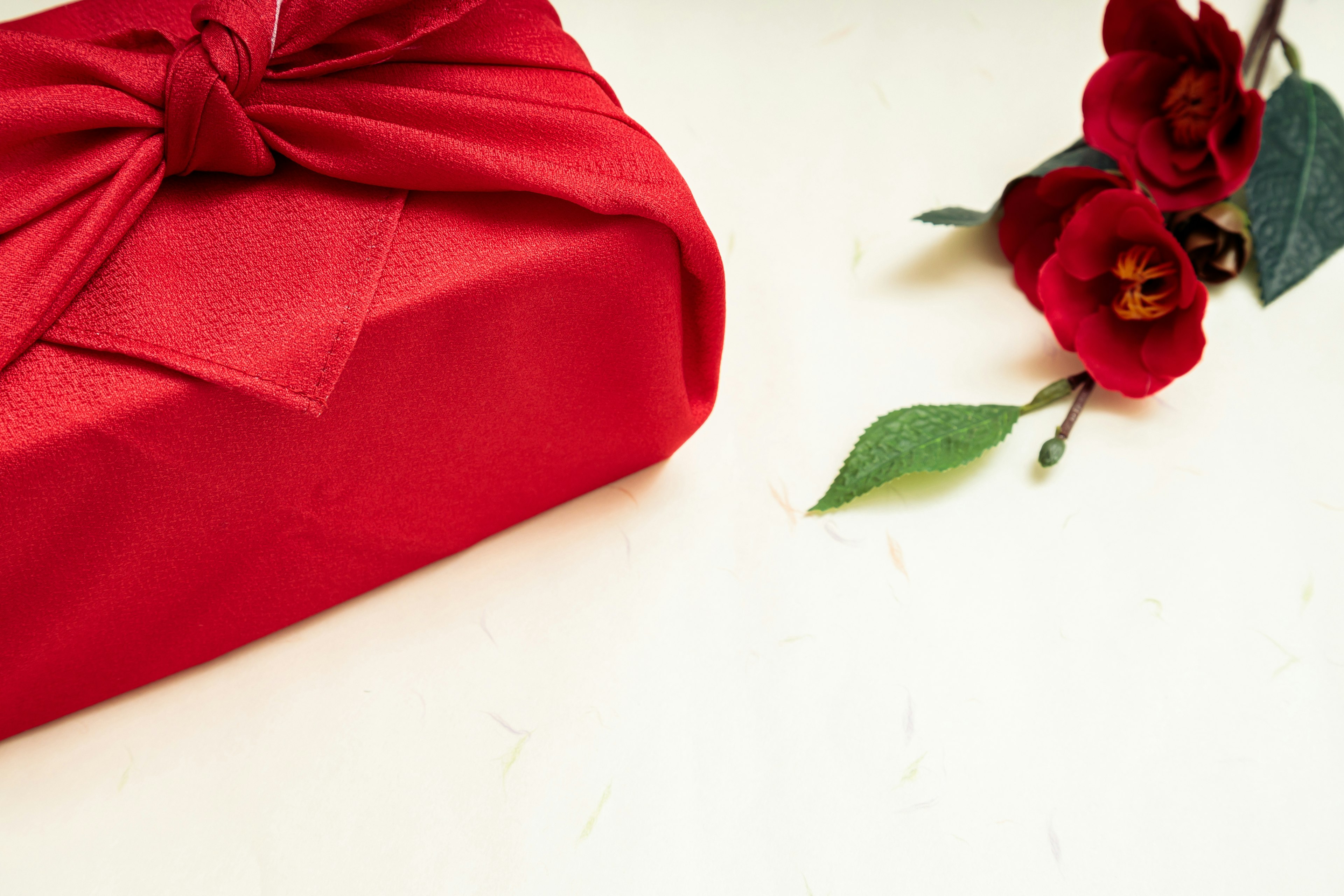 Red wrapped gift with a bow and red flowers on a simple background