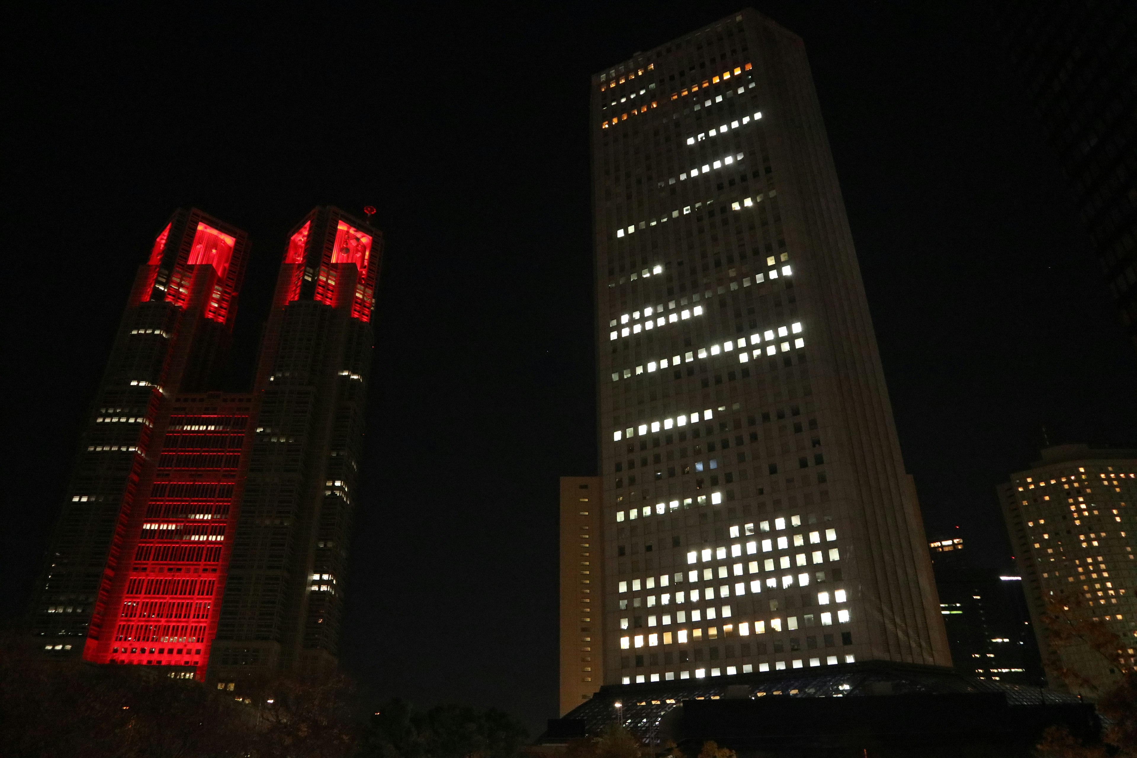 Tokyo skyscrapers at night featuring twin towers with red lights and brightly lit windows