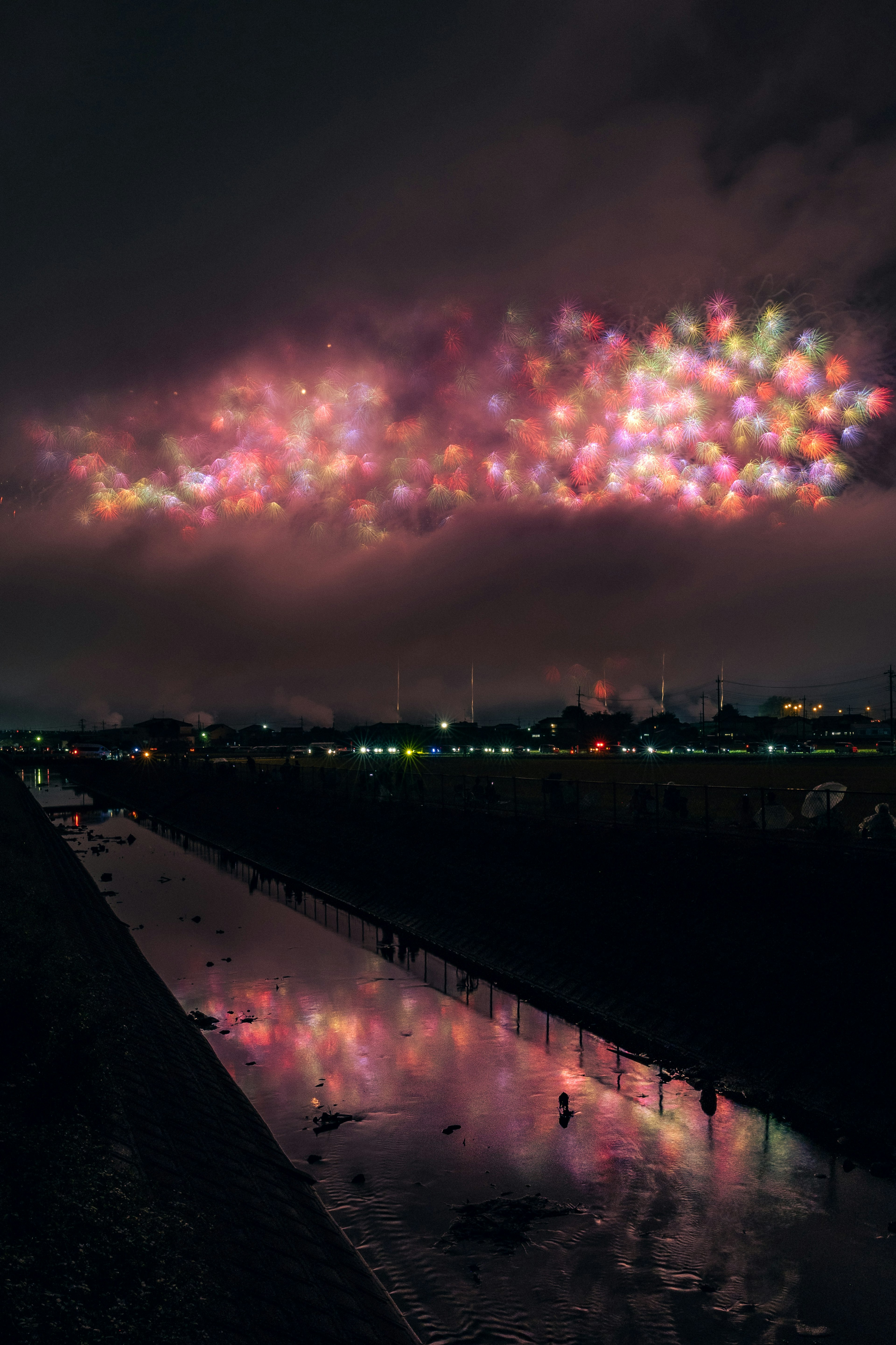 夜空に広がる色とりどりの光の雲と川の反射