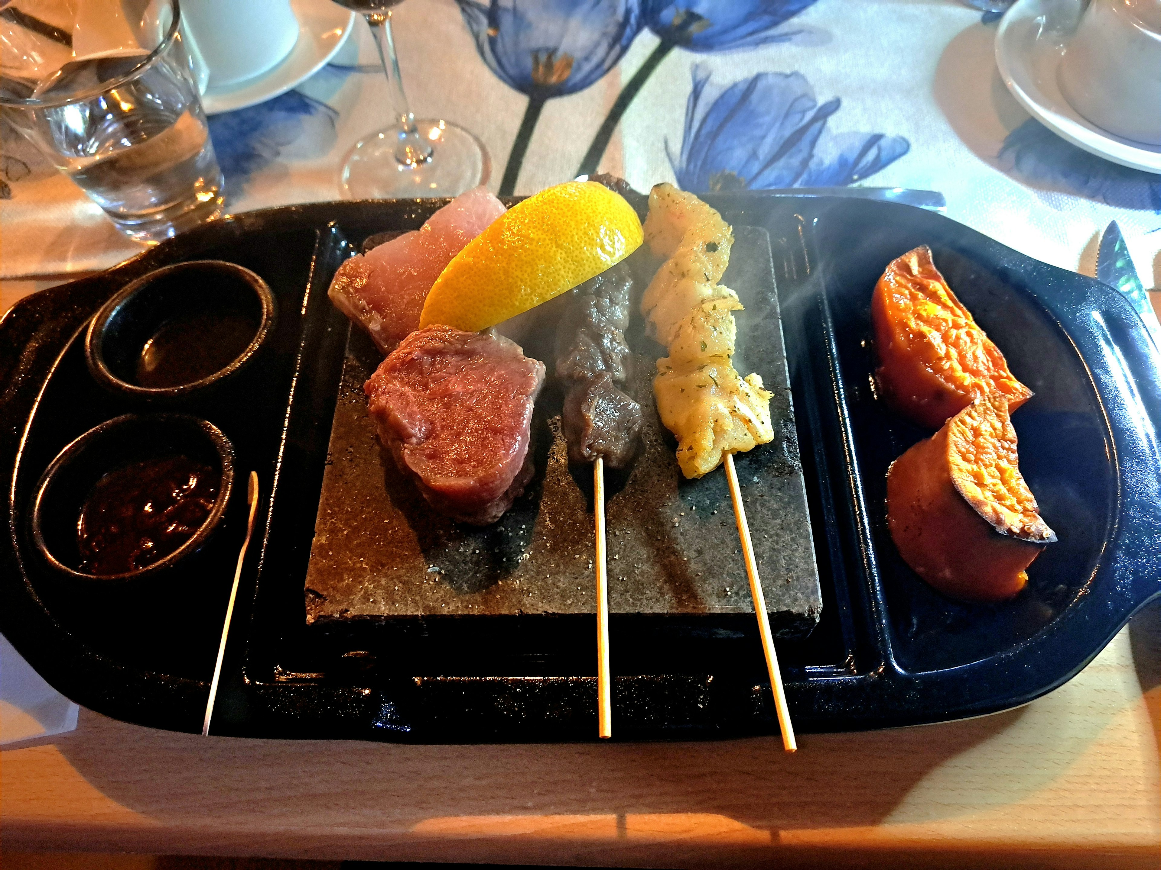 A beautiful plate of grilled meat and fish skewers served on a hot stone with dipping sauces