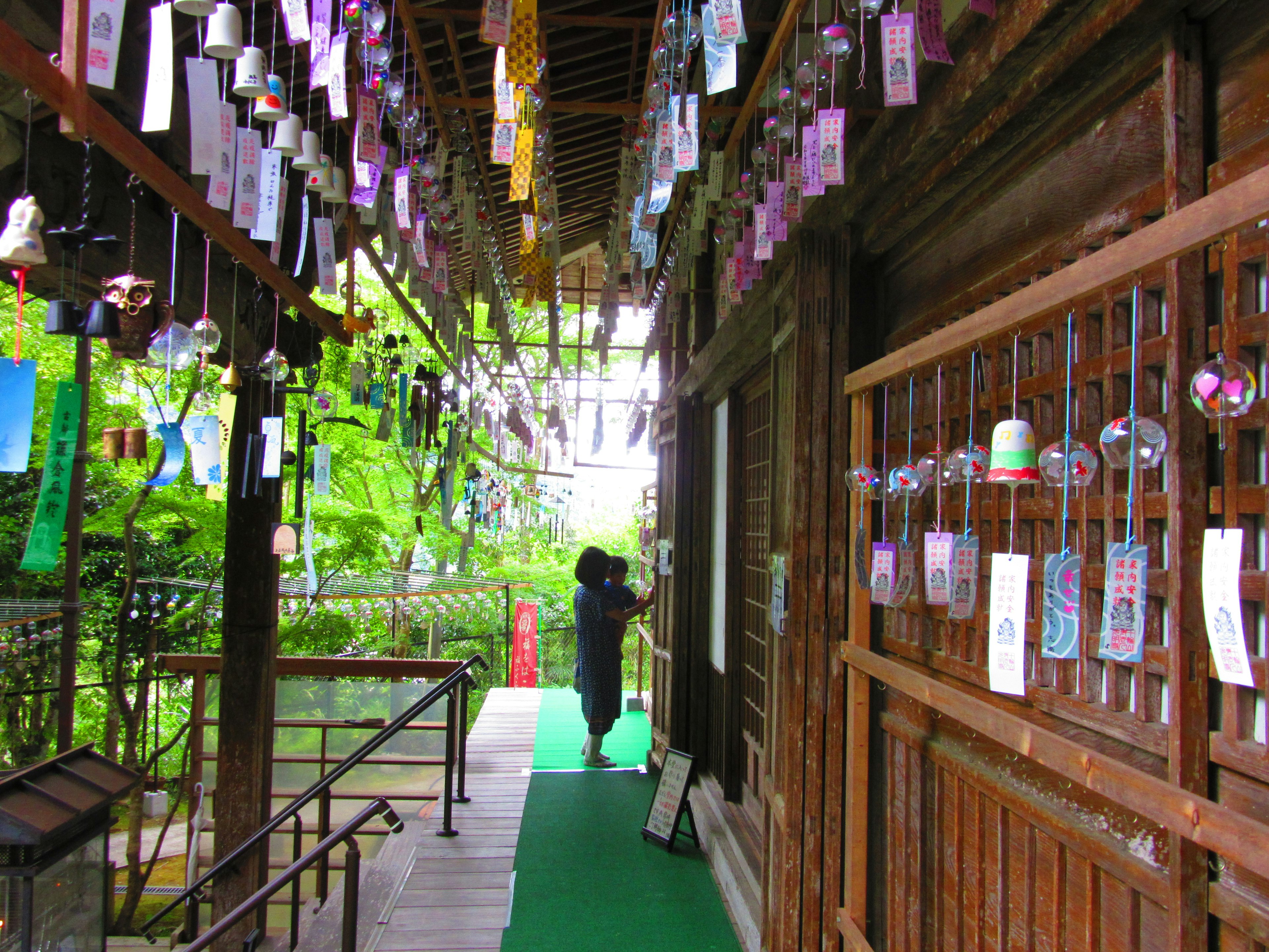 A scenic view of a wooden building with wind chimes hanging along a green pathway