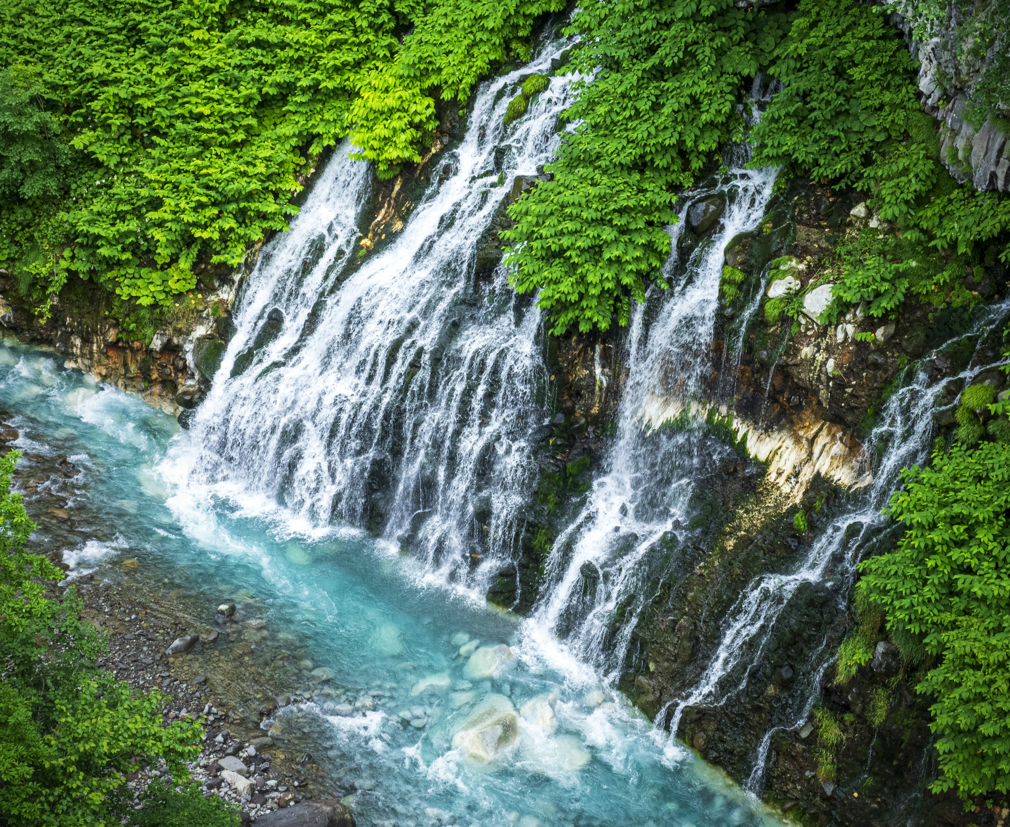 Una hermosa cascada que cae en un río turquesa rodeada de vegetación exuberante