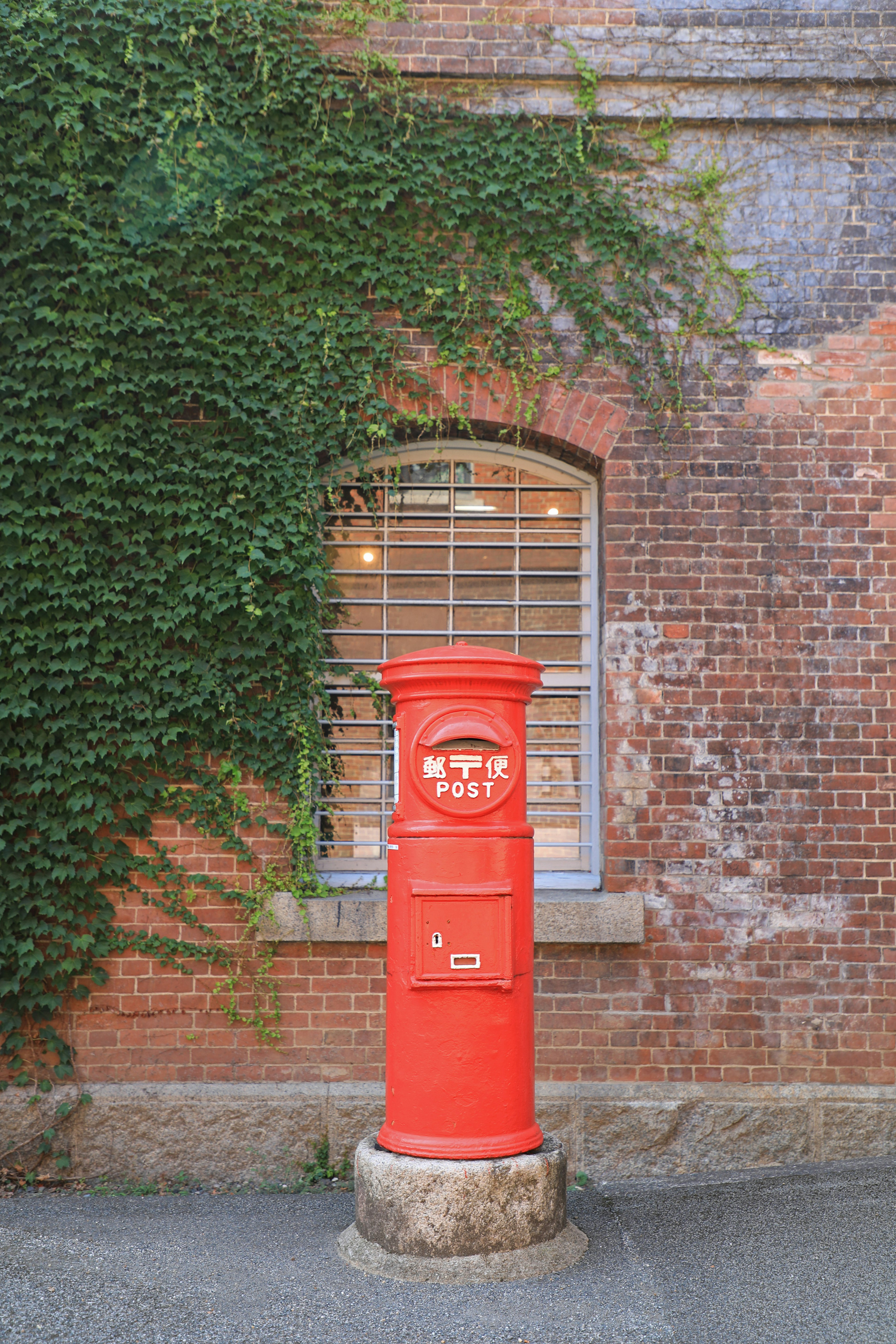 Boîte aux lettres rouge devant un mur en brique avec de la vigne verte