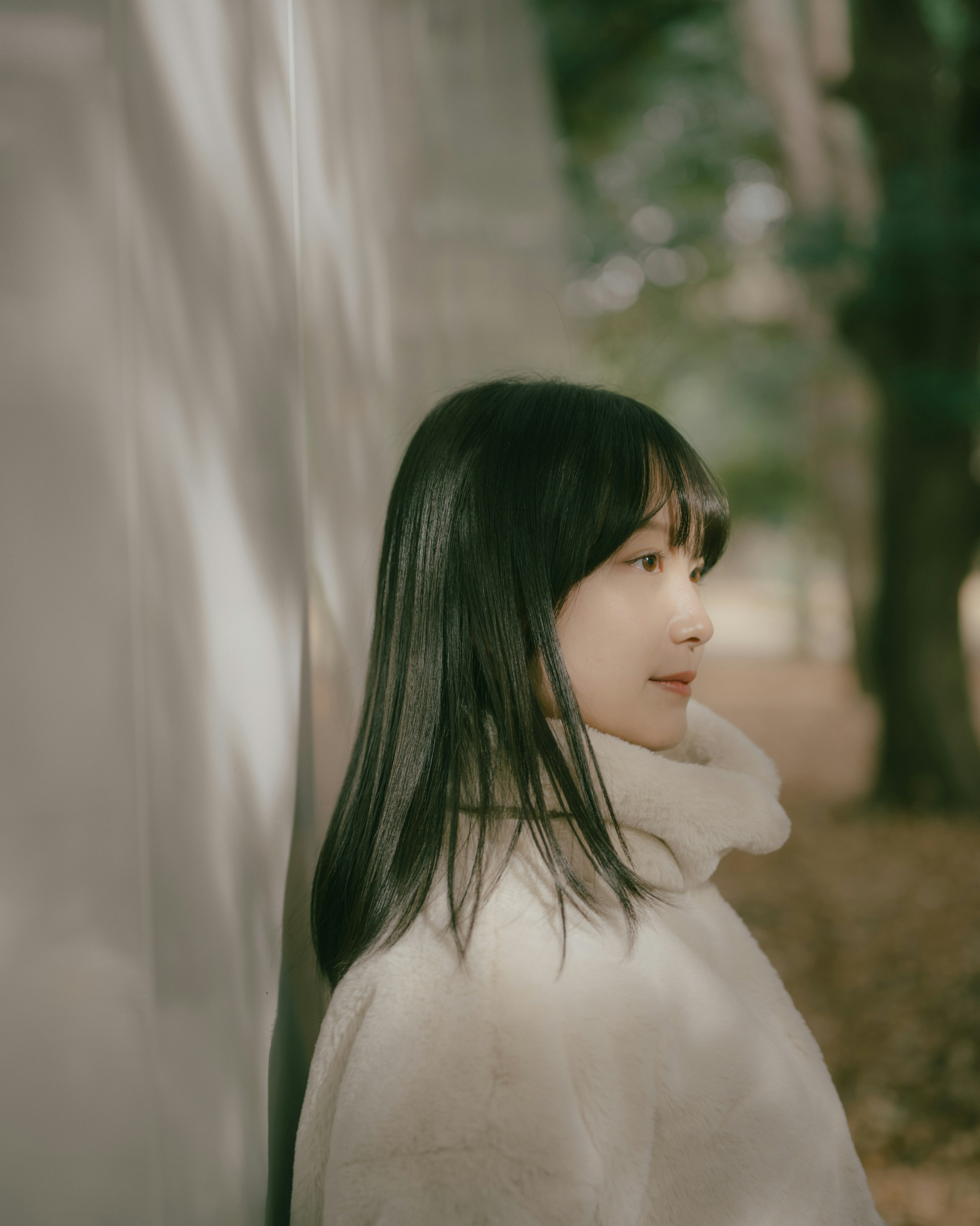 A woman in a white coat leaning against a wall