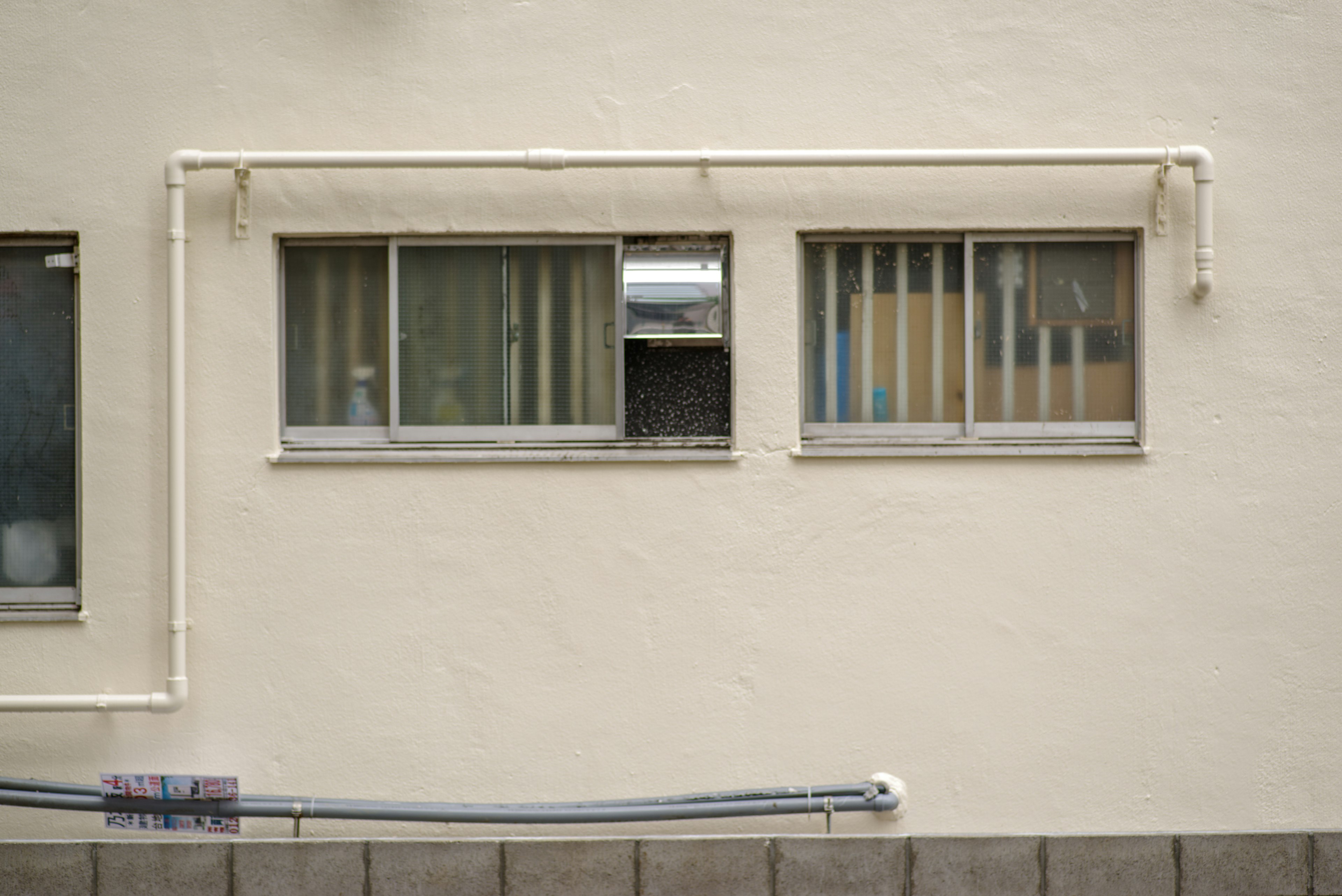 Extérieur d'un bâtiment avec deux fenêtres et des tuyaux visibles sur un mur blanc