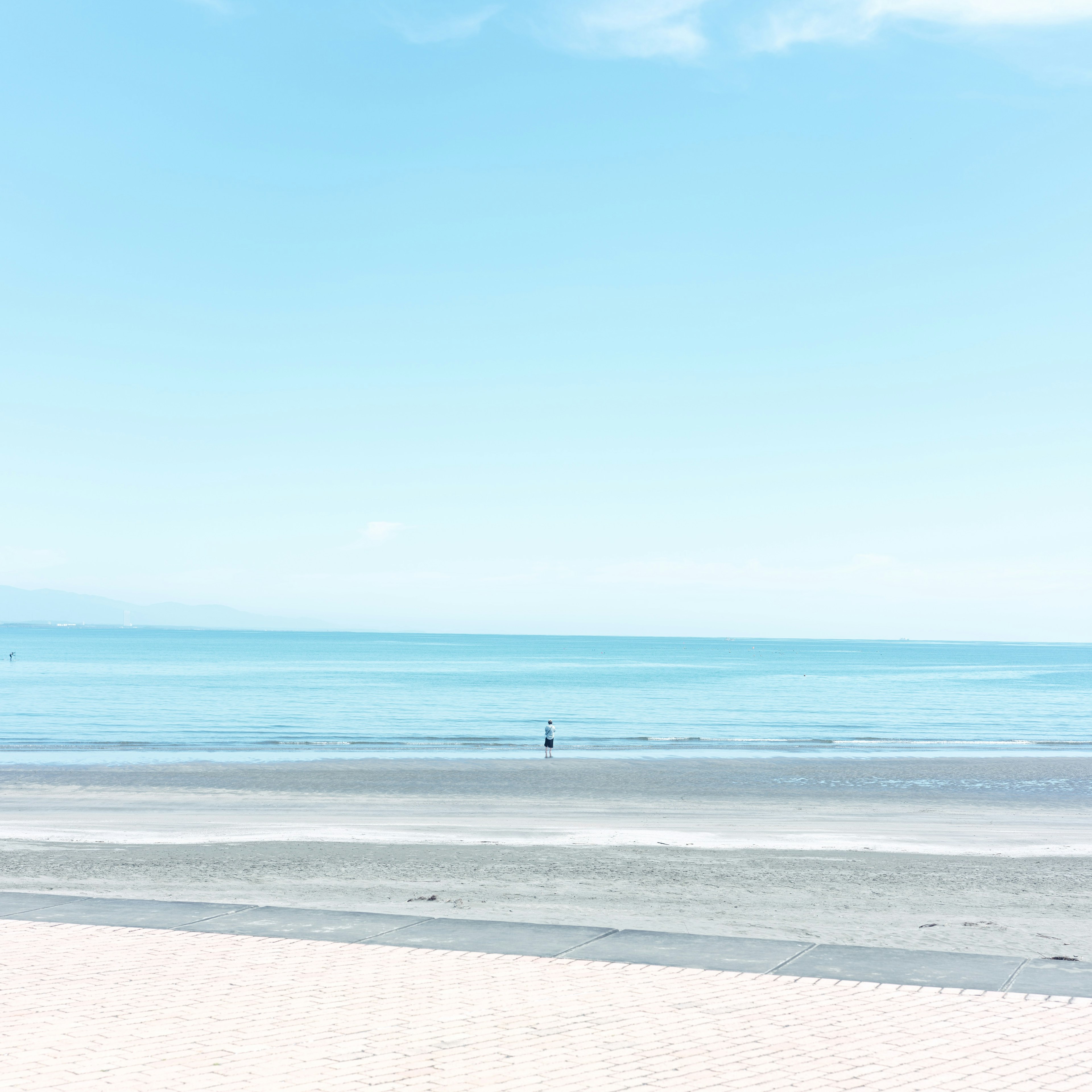 穏やかな青い海と空が広がるビーチの風景 一人の人が遠くに立っている