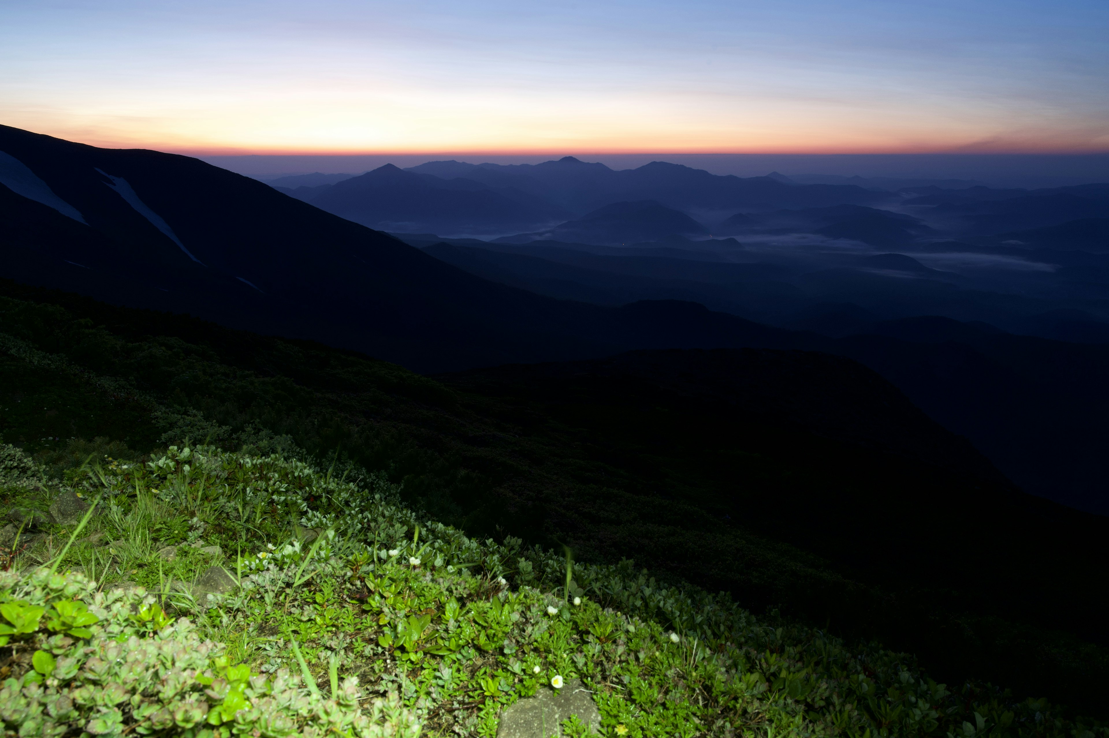 Pemandangan senja dengan pegunungan dan rumput hijau