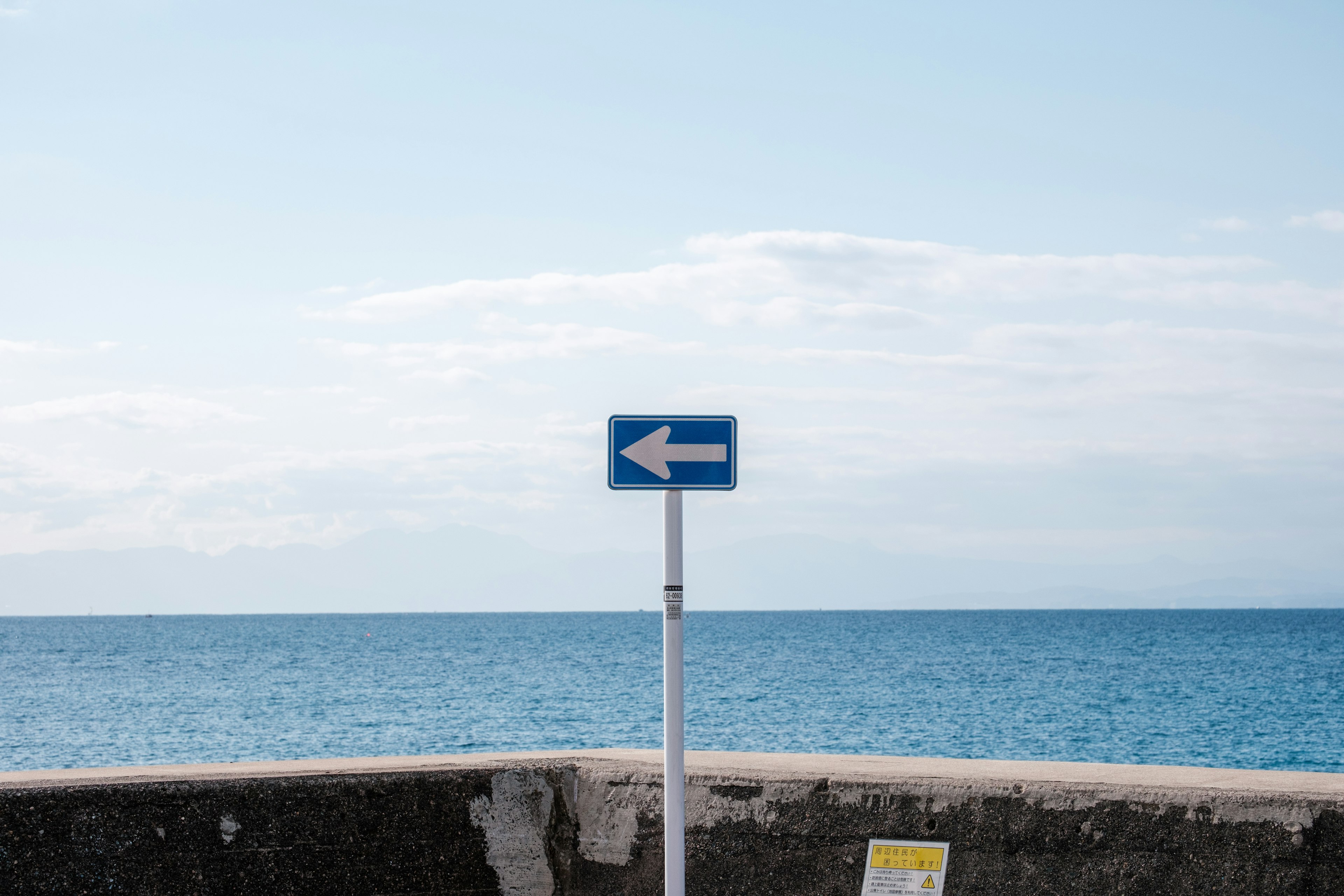 Panneau bleu fléché à gauche avec une mer calme en arrière-plan