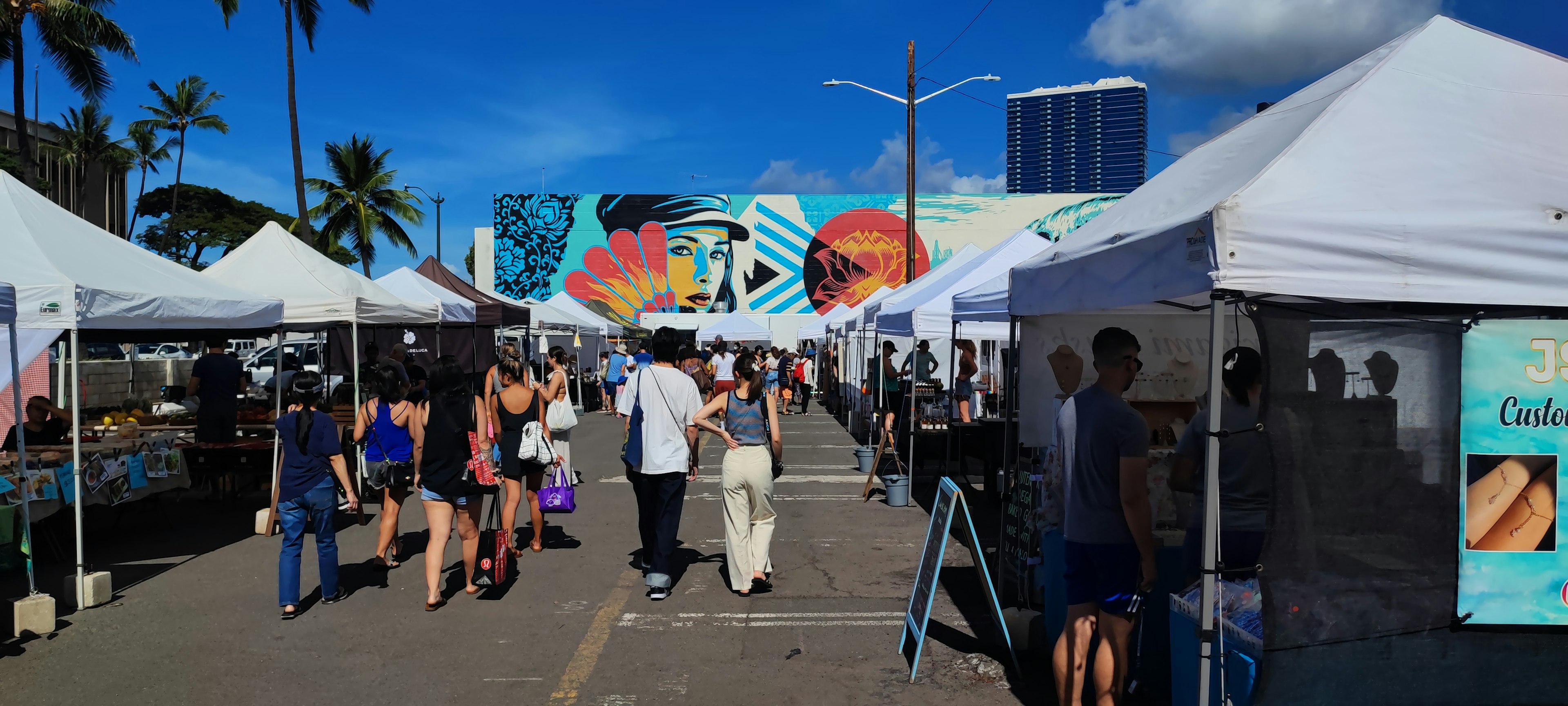 Scène de marché en plein air avec une fresque colorée en arrière-plan de nombreux stands et visiteurs animés