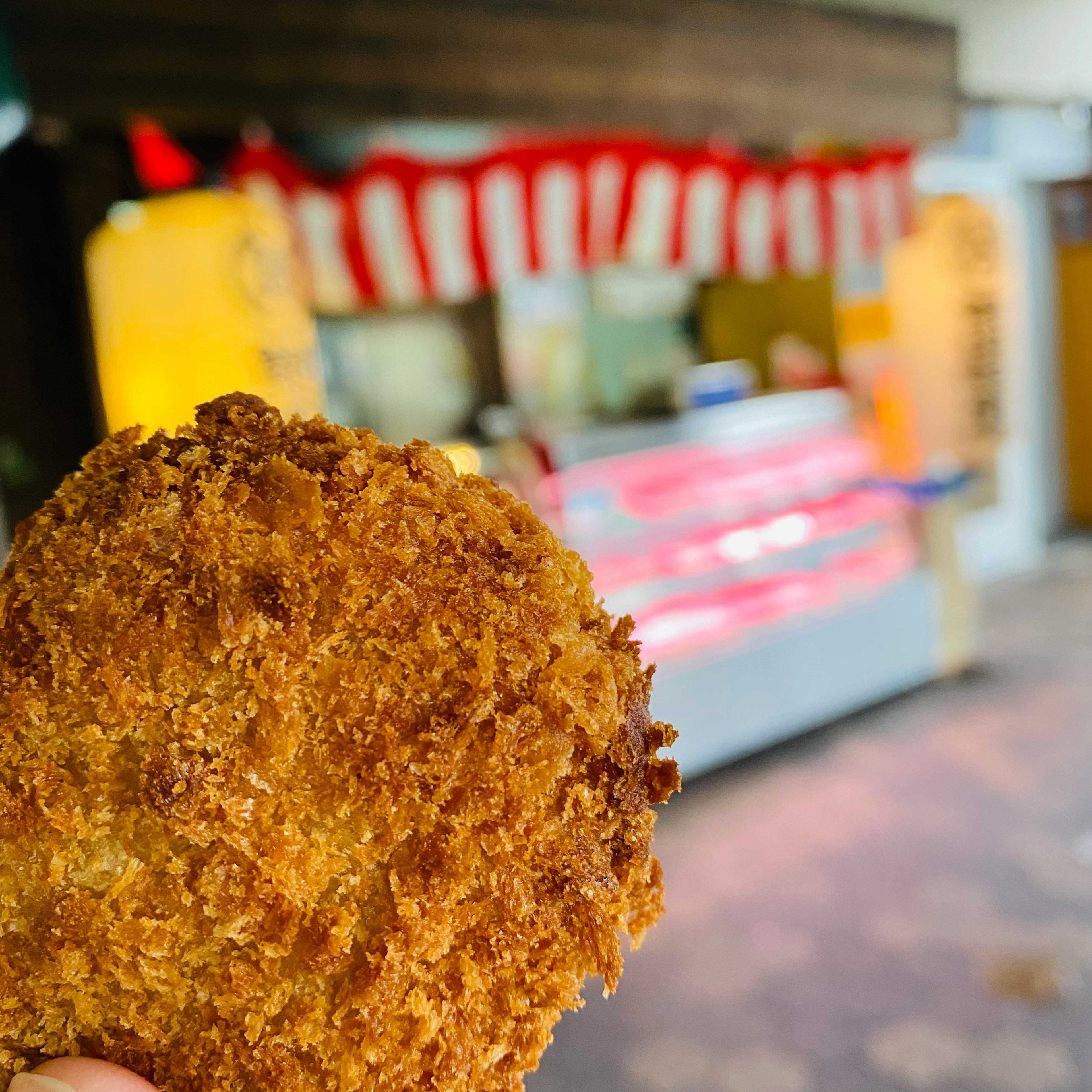 Ein frisch gebratenes Kroketten in der Hand mit einem Essensstand im Hintergrund