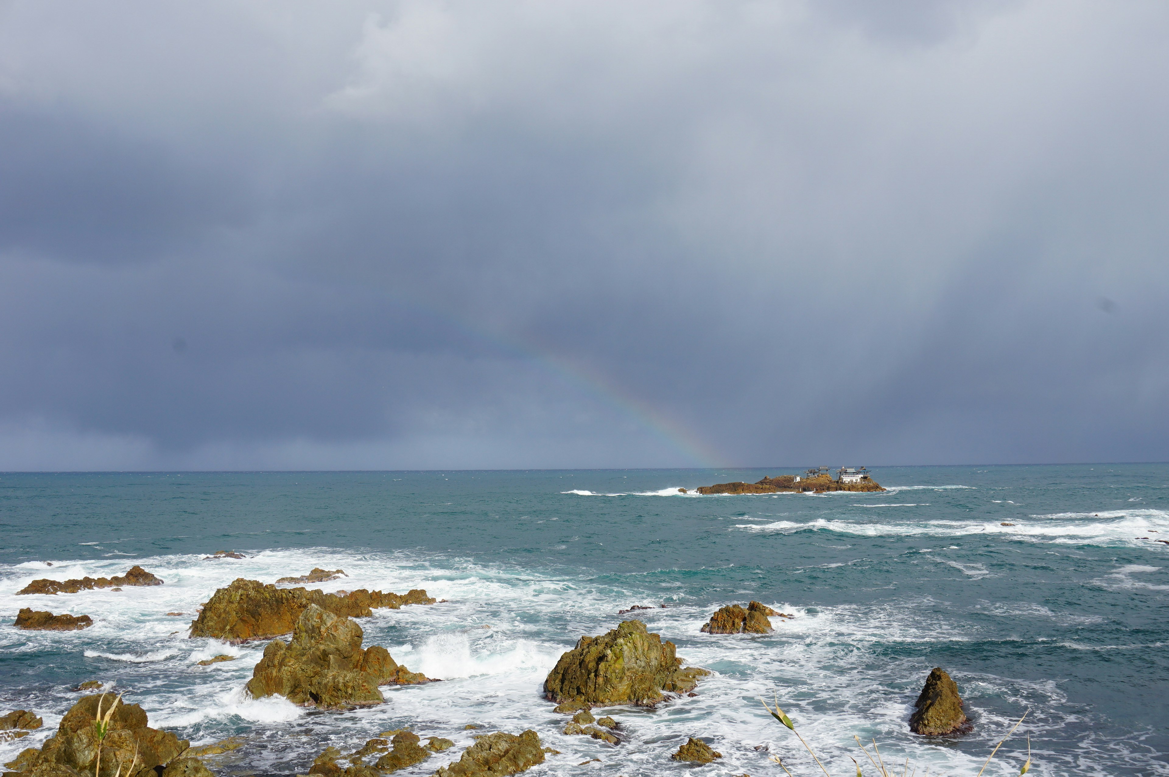 Costa rocosa con mar agitado cielo nublado oscuro con un faro a lo lejos