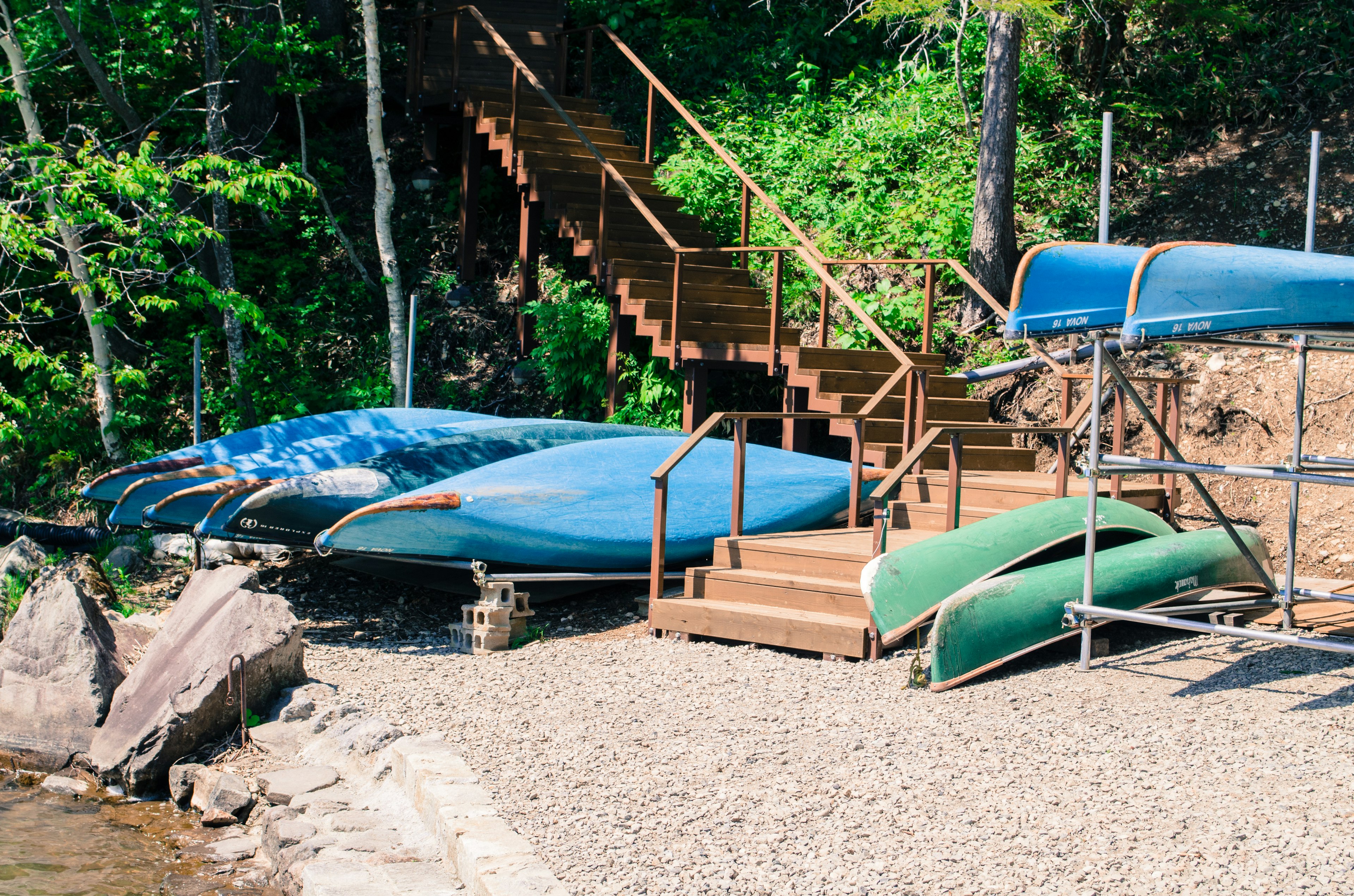 Blue canoe and green kayak on a lakeside with wooden stairs in the background