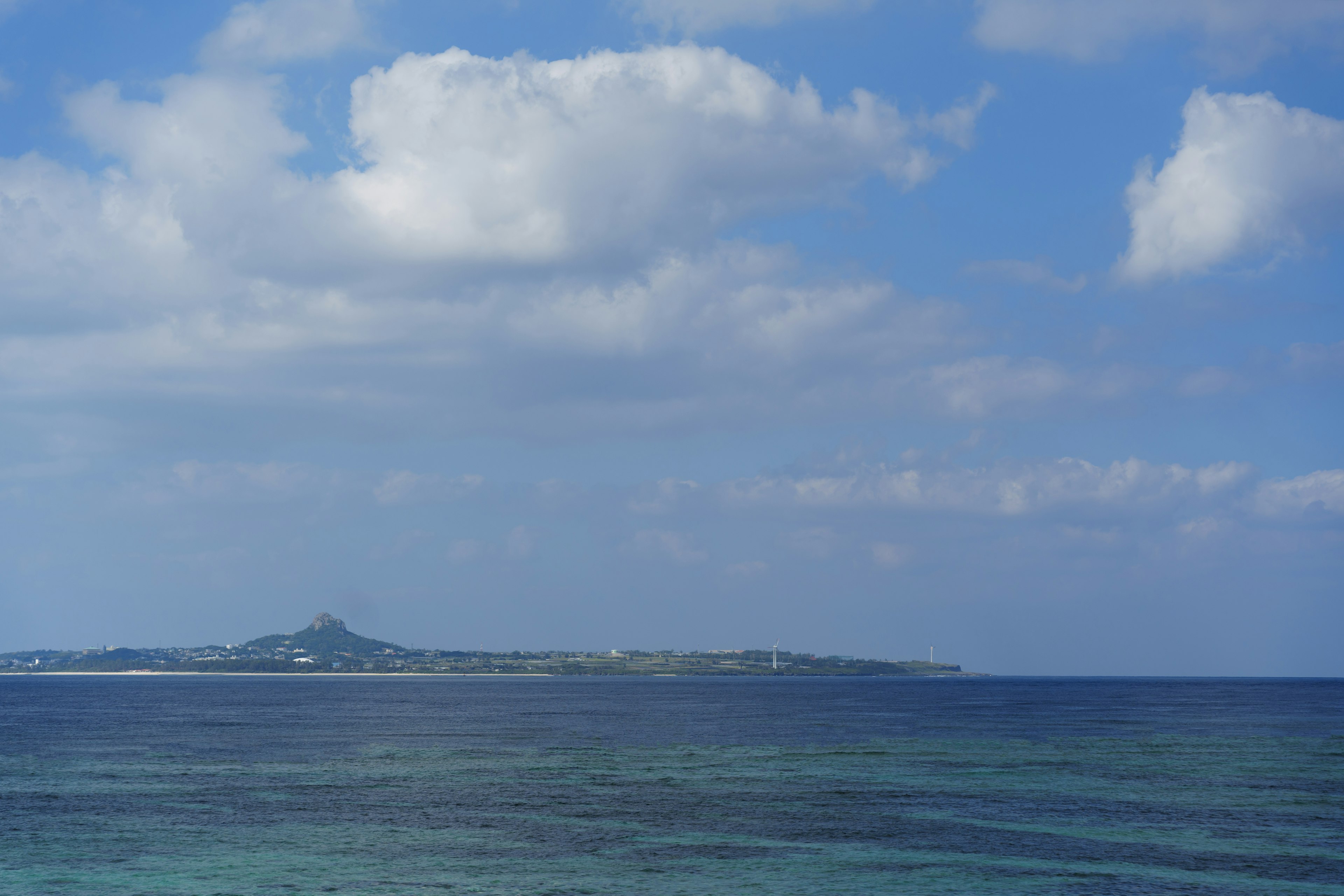 Scenic view of an island under a blue sky with white clouds