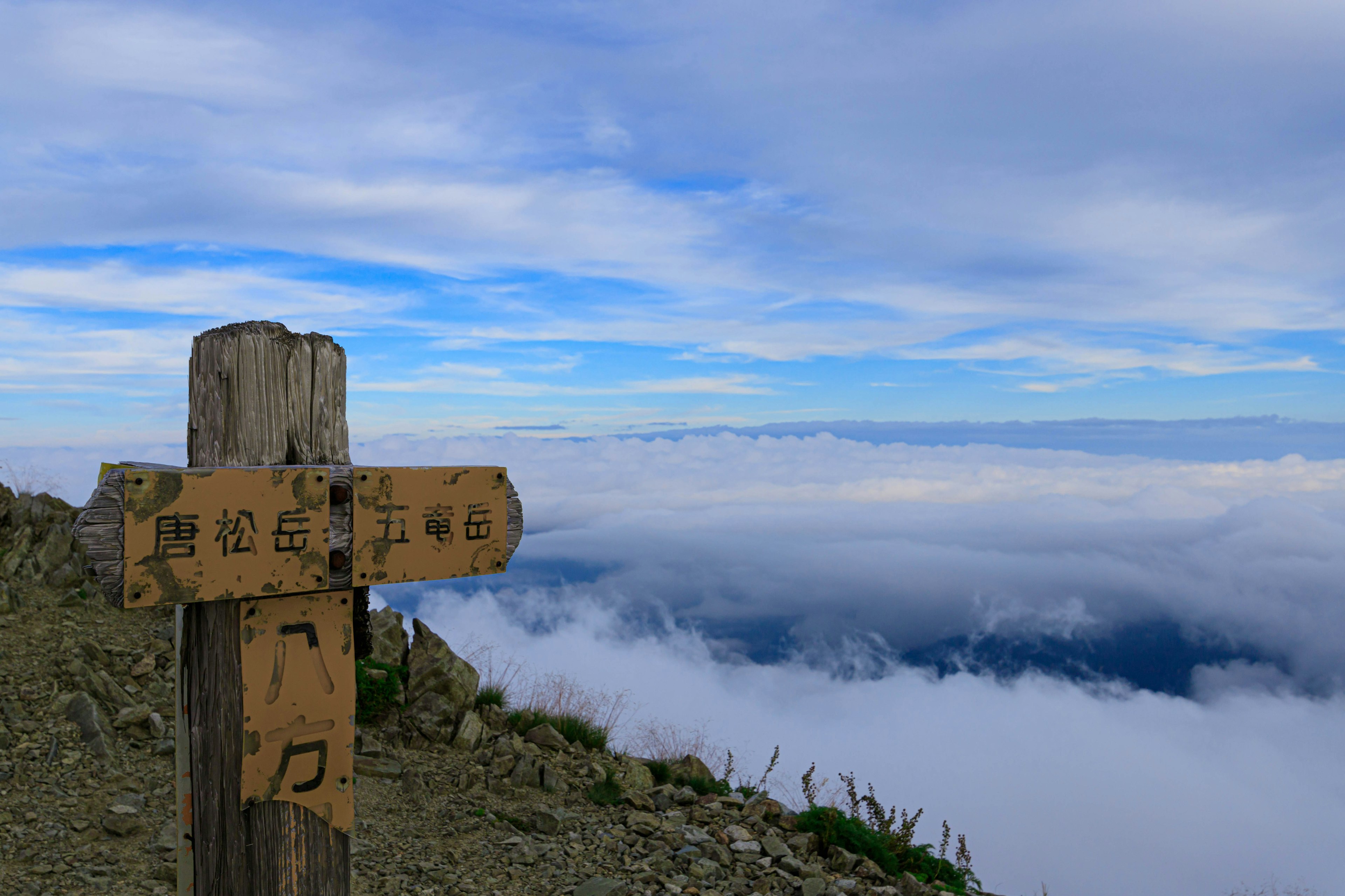 Cartello di legno sulla cima della montagna che sovrasta un mare di nuvole