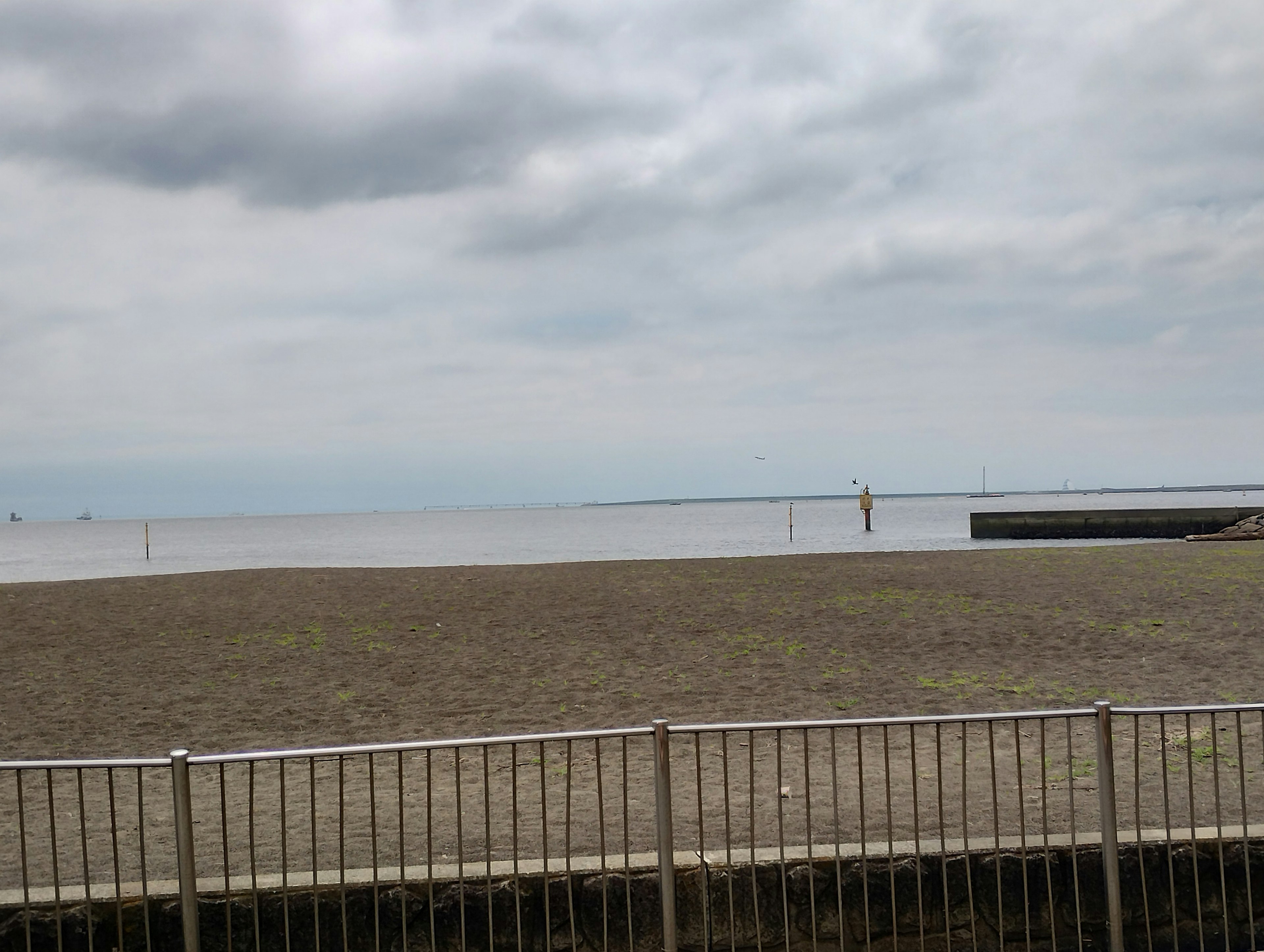 Pantai pasir yang luas dengan laut tenang di bawah langit mendung menunjukkan pemandangan pantai yang tenang