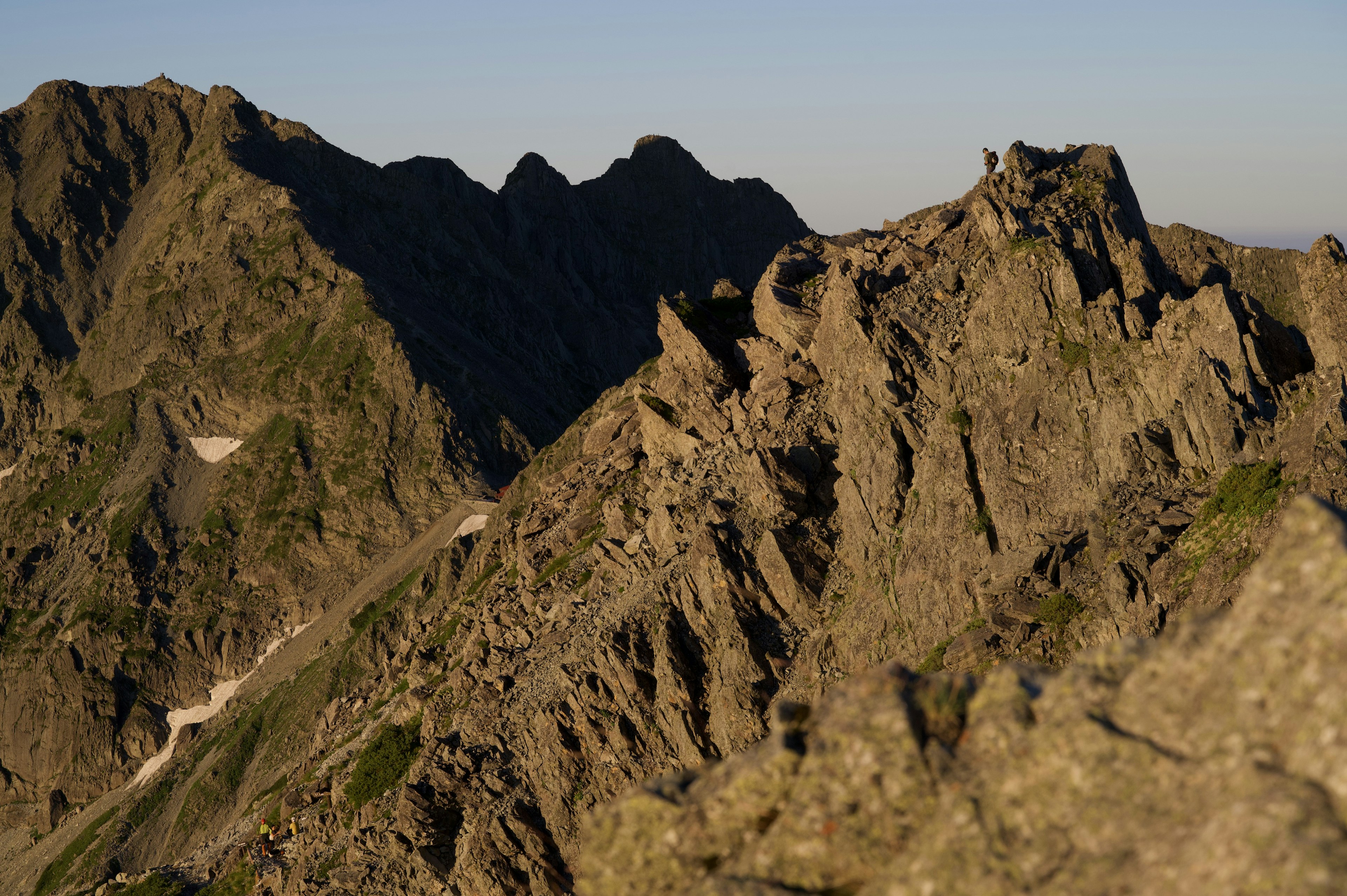 Formaciones rocosas afiladas en la cima de una montaña con sombras de montañas distantes