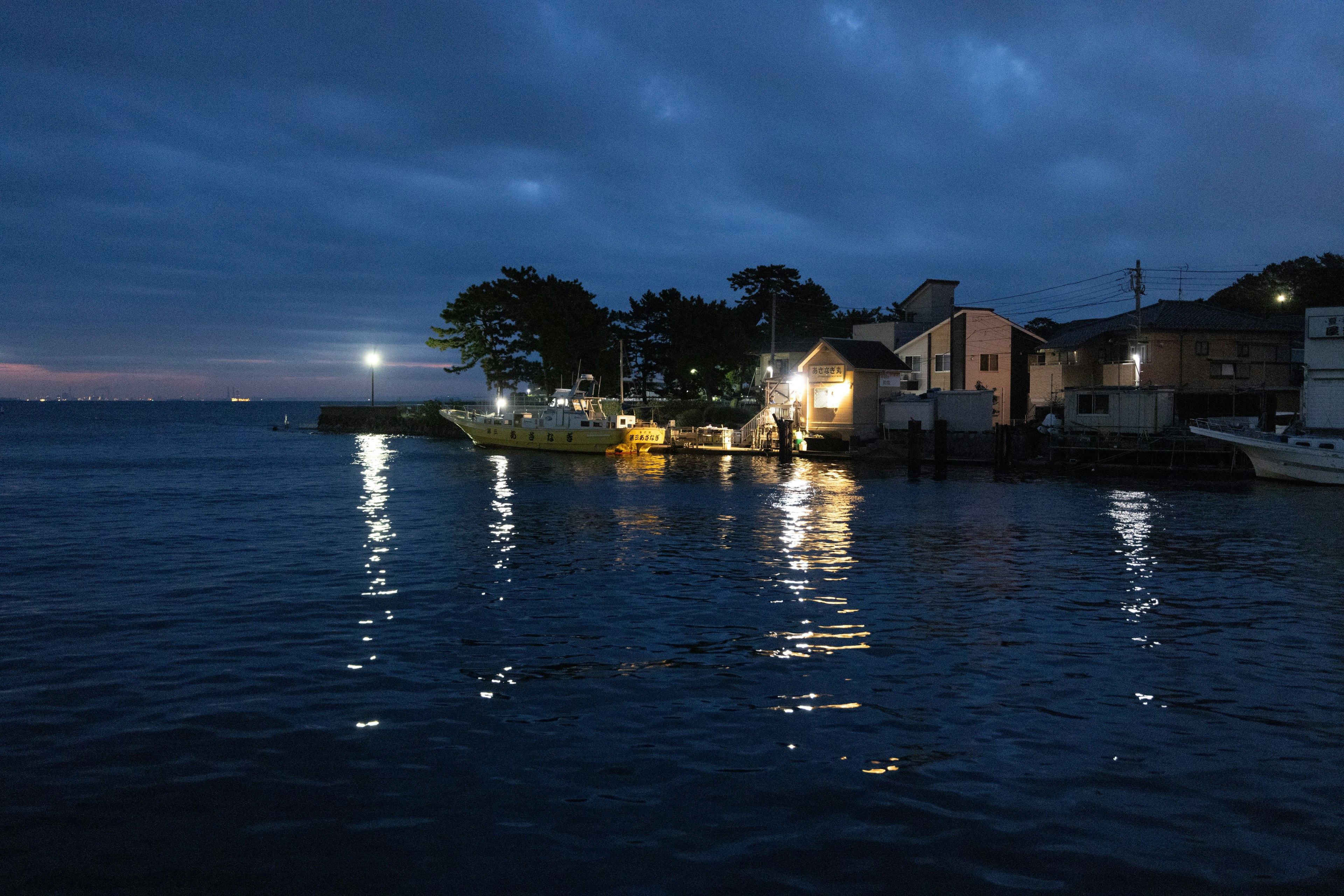 Nachtszene eines Fischerdorfes mit Lichtern, die sich auf dem ruhigen Meer spiegeln
